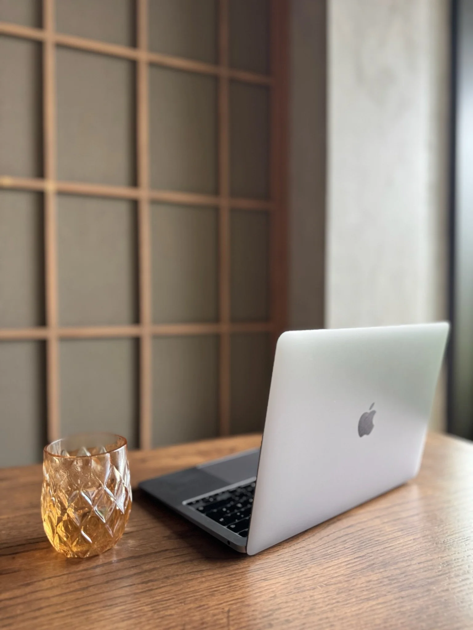Ein offener Laptop auf einem Holztisch mit einem Goldfarbenen Glas und einem weißen Stuhl im Hintergrund.