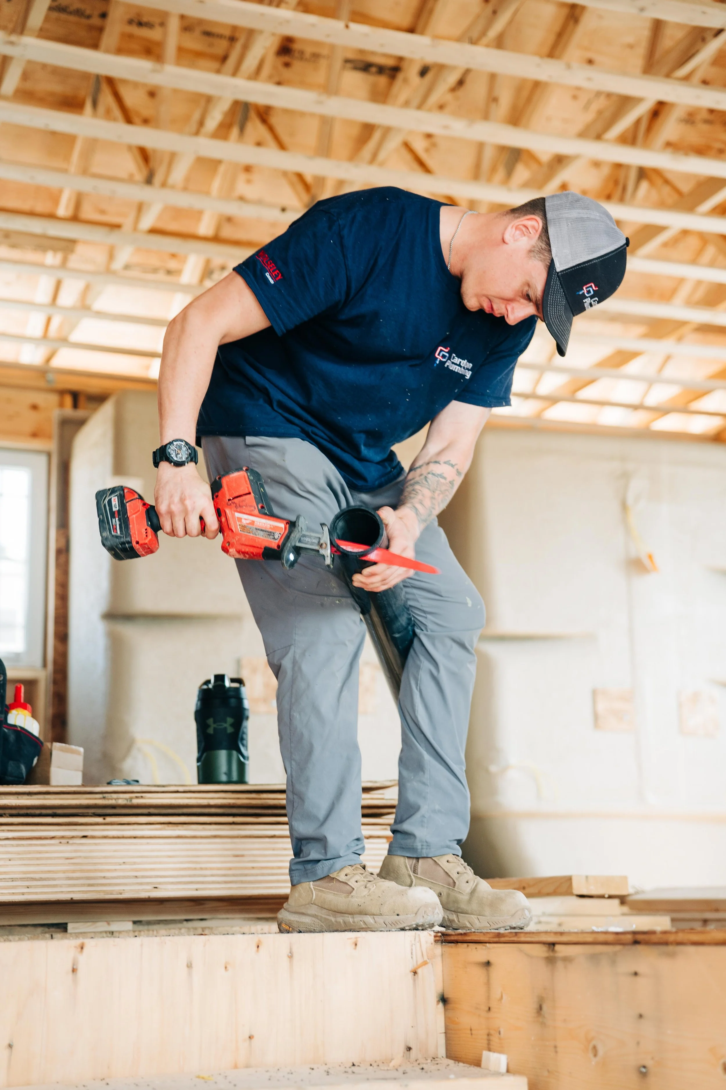 A man working on construction inside a wooden building frame, holding a power drill.