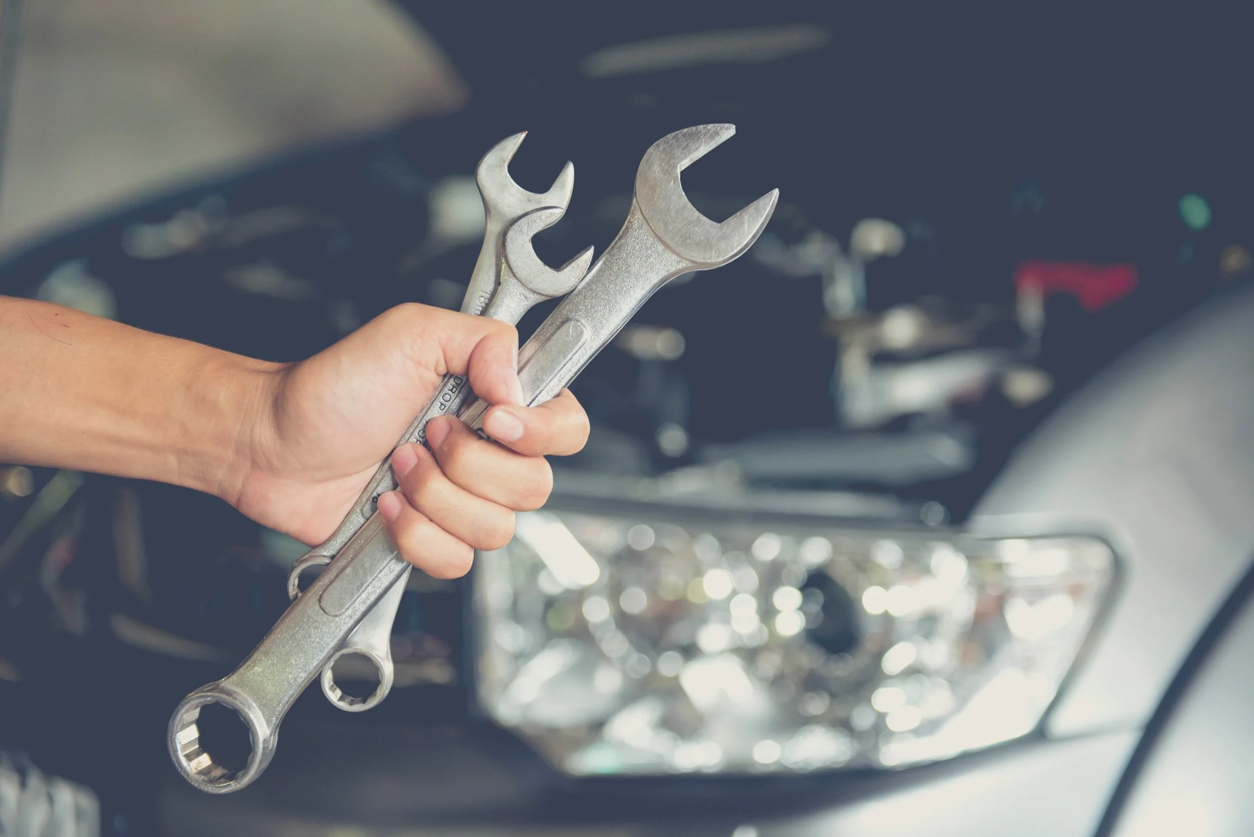 Nahaufnahme eines menschlichen Arms, der zwei Schraubenschlüssel hält, während im Hintergrund mehrere Motorräder stehen.