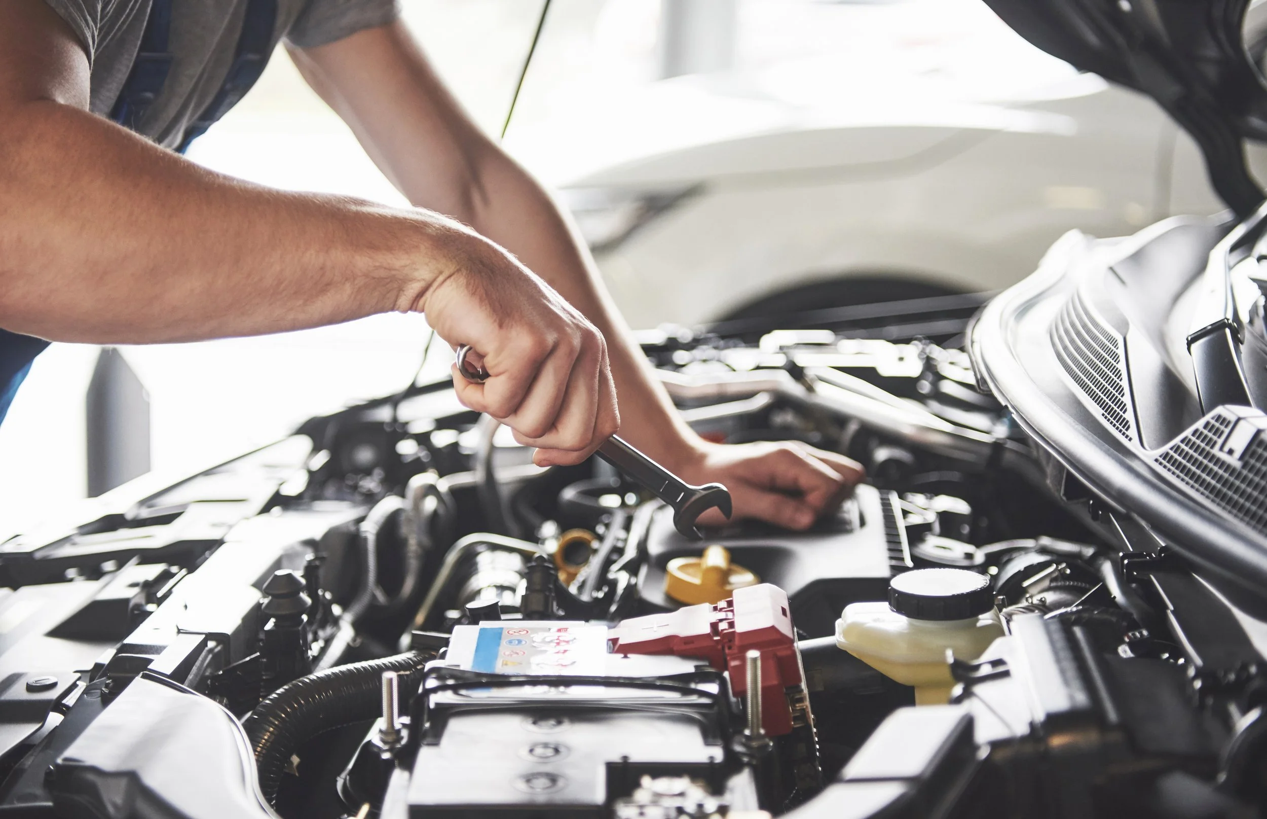 Eine Person arbeitet im Motorraum eines Autos, hält einen Schraubenschlüssel in der Hand und arbeitet an den Fahrzeugkomponenten.