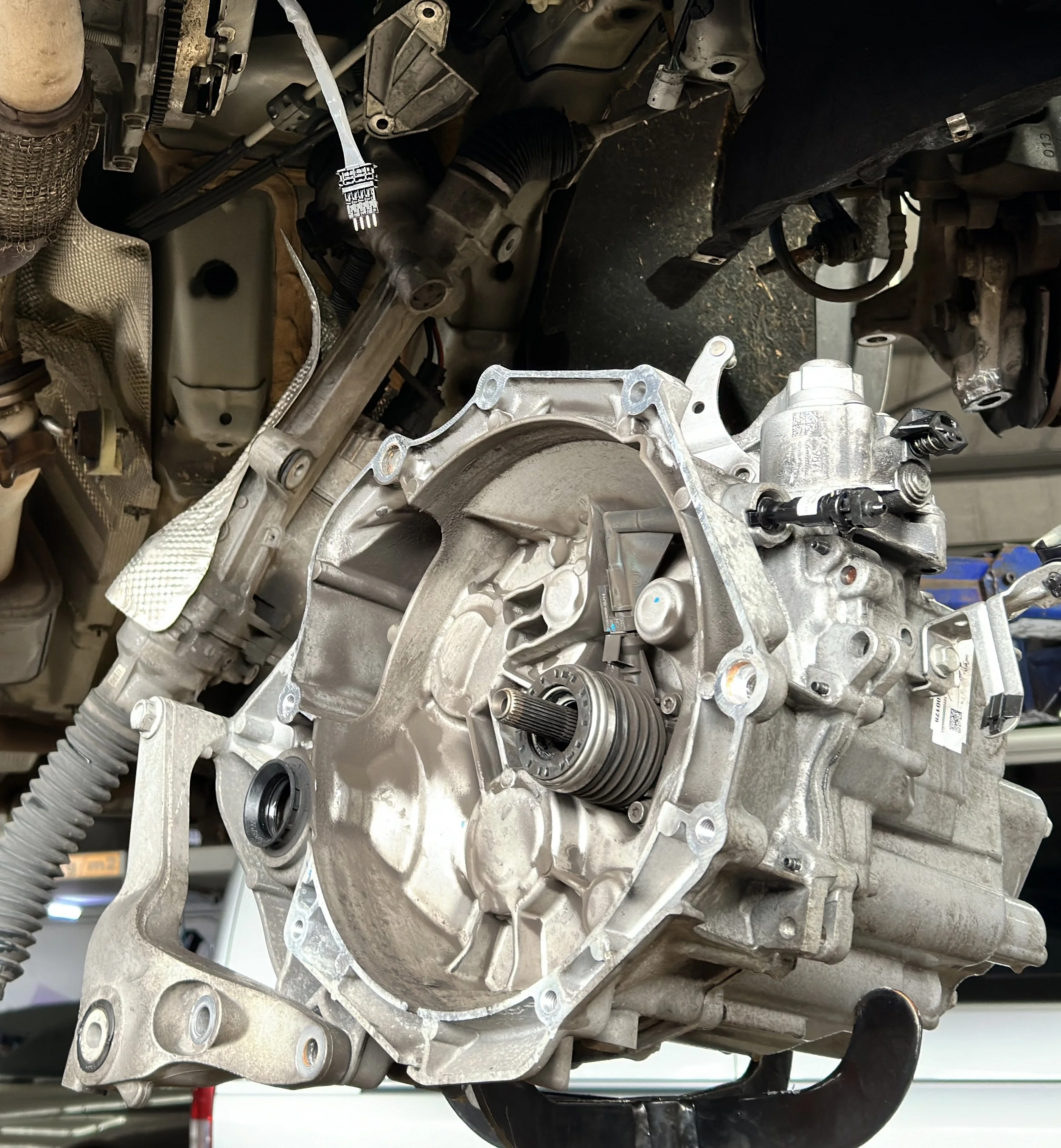 Nahaufnahme eines Automotorblocks, sichtbar sind metallische Bauteile, Zahnräder, Riemenscheiben und Schläuche.