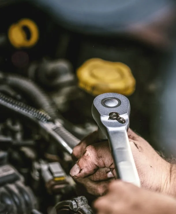 Hand eines Mechanikers bei der Reparatur eines Autos, Verwendung eines Schraubenschlüssels im Motorraum.