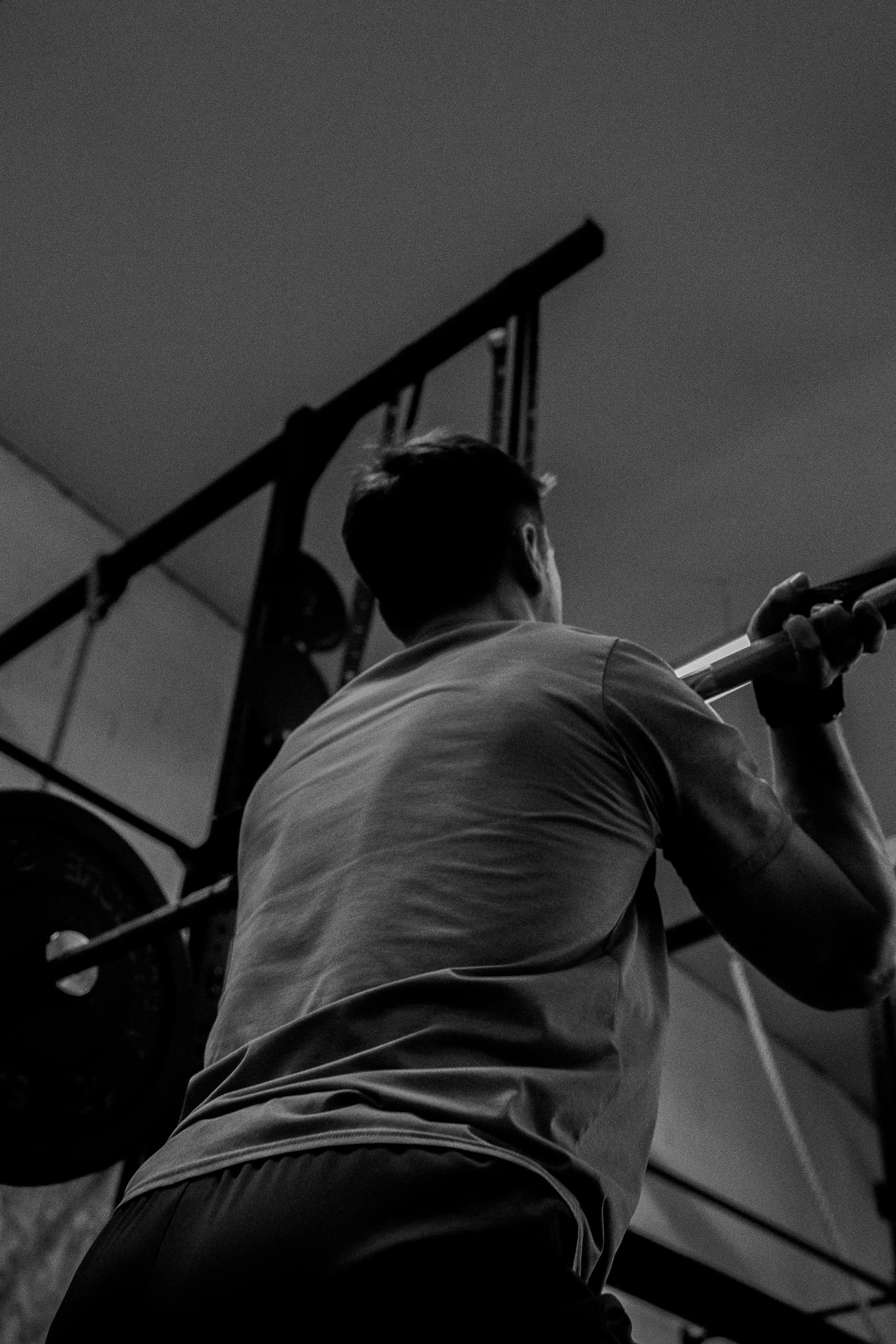Une personne s'entraînant avec une barre sous un rack à la salle de sport, vue de dos en noir et blanc.