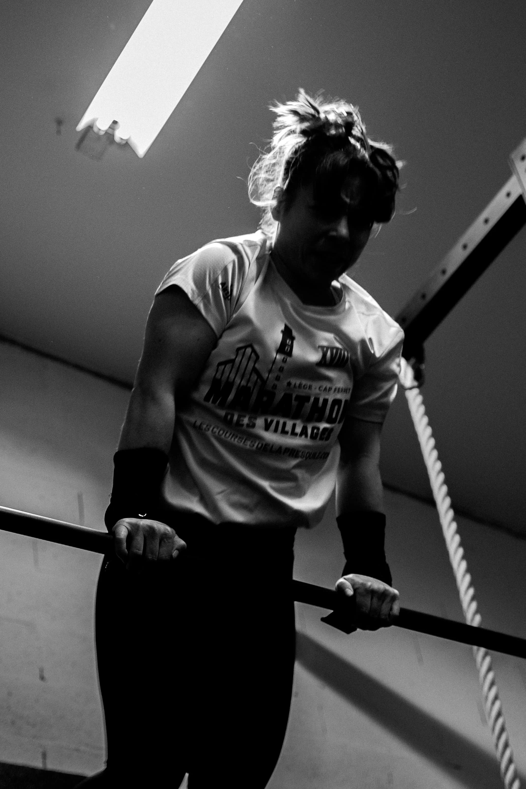 Une femme en tshirt participant à un entraînement de marche sur corde à l'intérieur, vue de profil, accrochée à une barre, en noir et blanc.