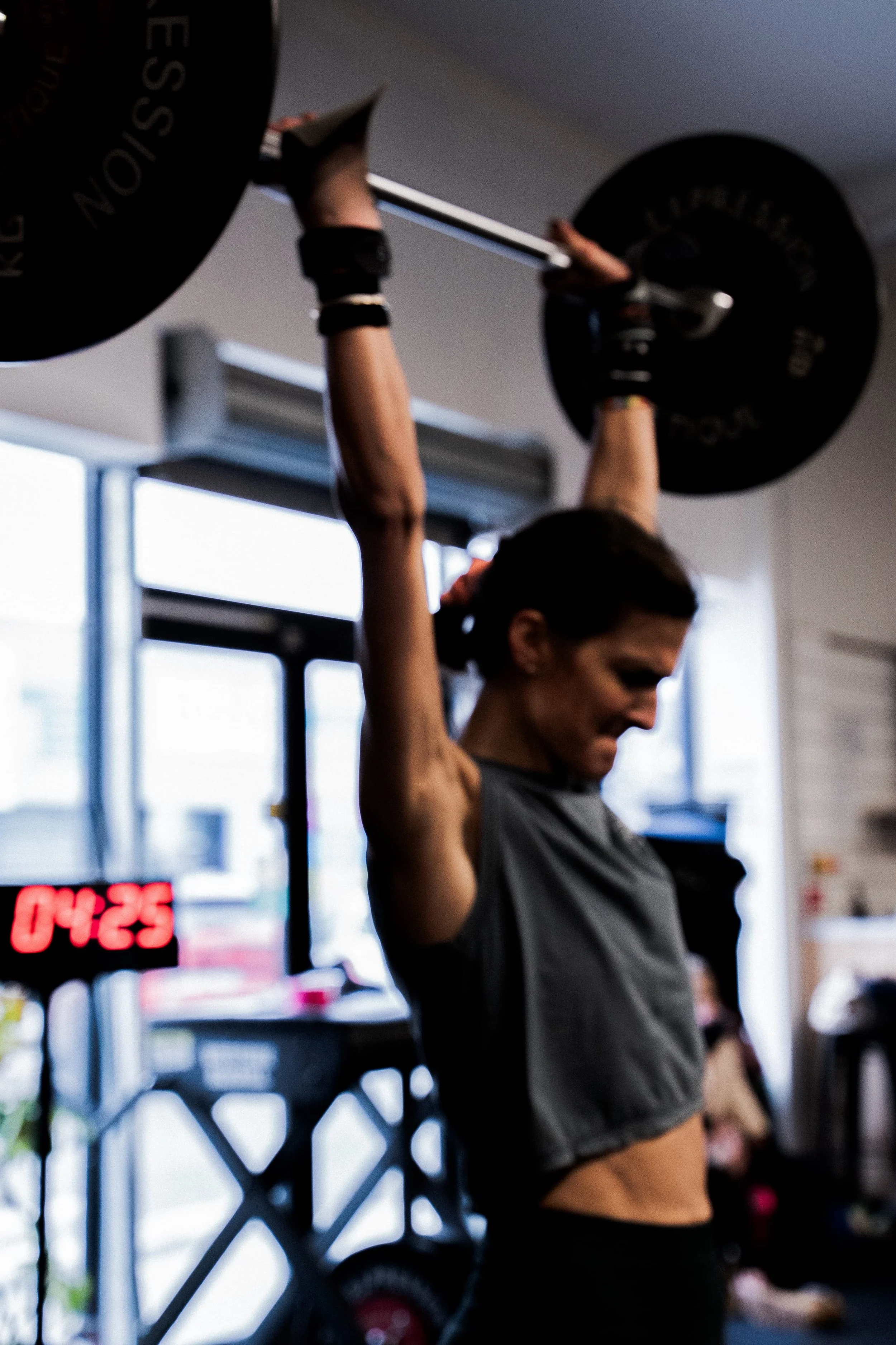 Une femme faisant de l'haltérophilie au gymnase, soulevant une barre avec des poids.