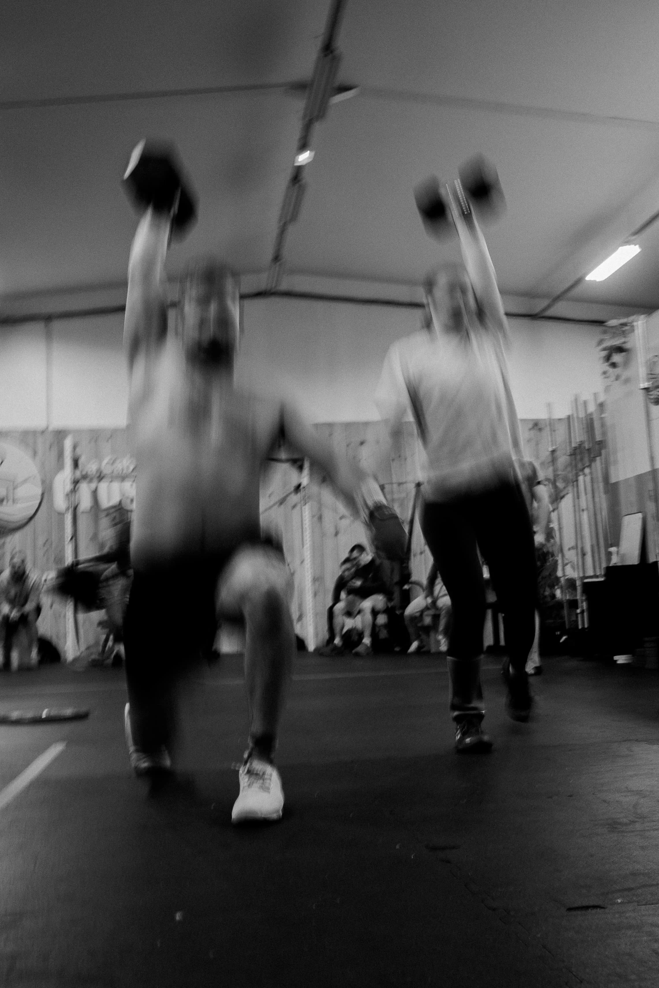 Deux hommes effectuent des figures acrobatiques dans une salle de gymnastique, avec un public en arrière-plan.