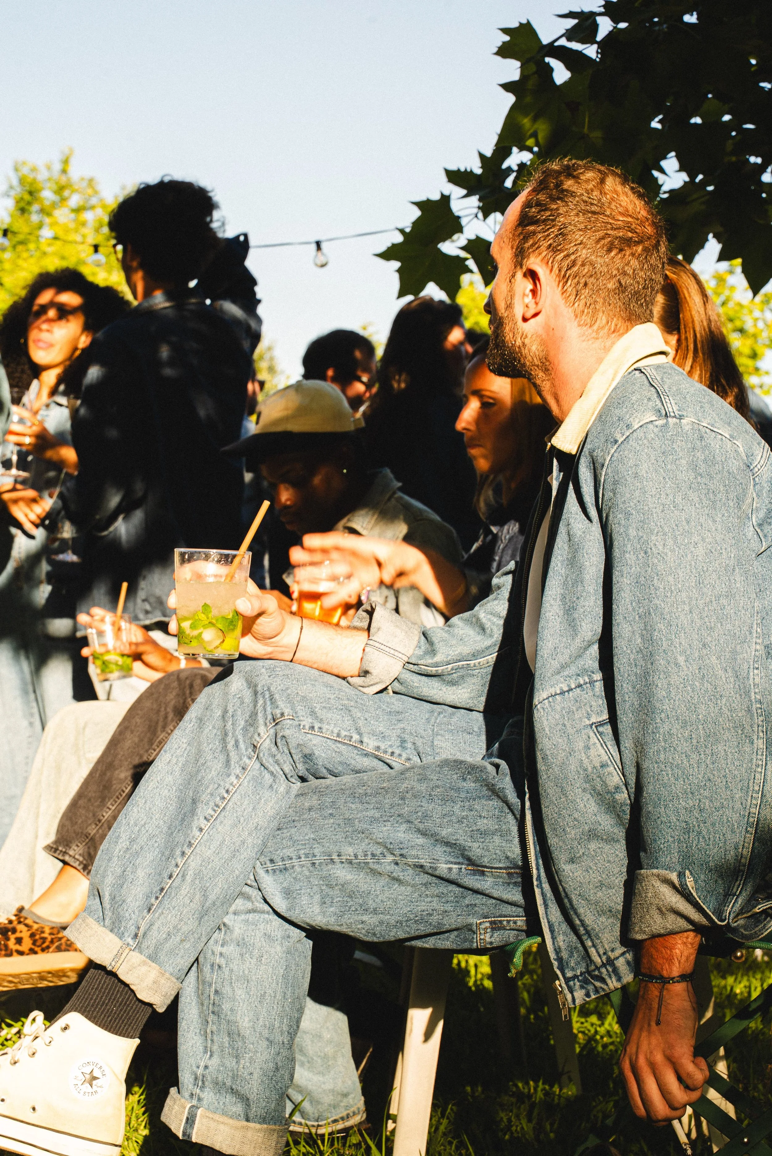 Groupe de personnes lors d'une rencontre en plein air, portant des vêtements décontractés et tenant des boissons. L'ambiance semble conviviale et détendue.