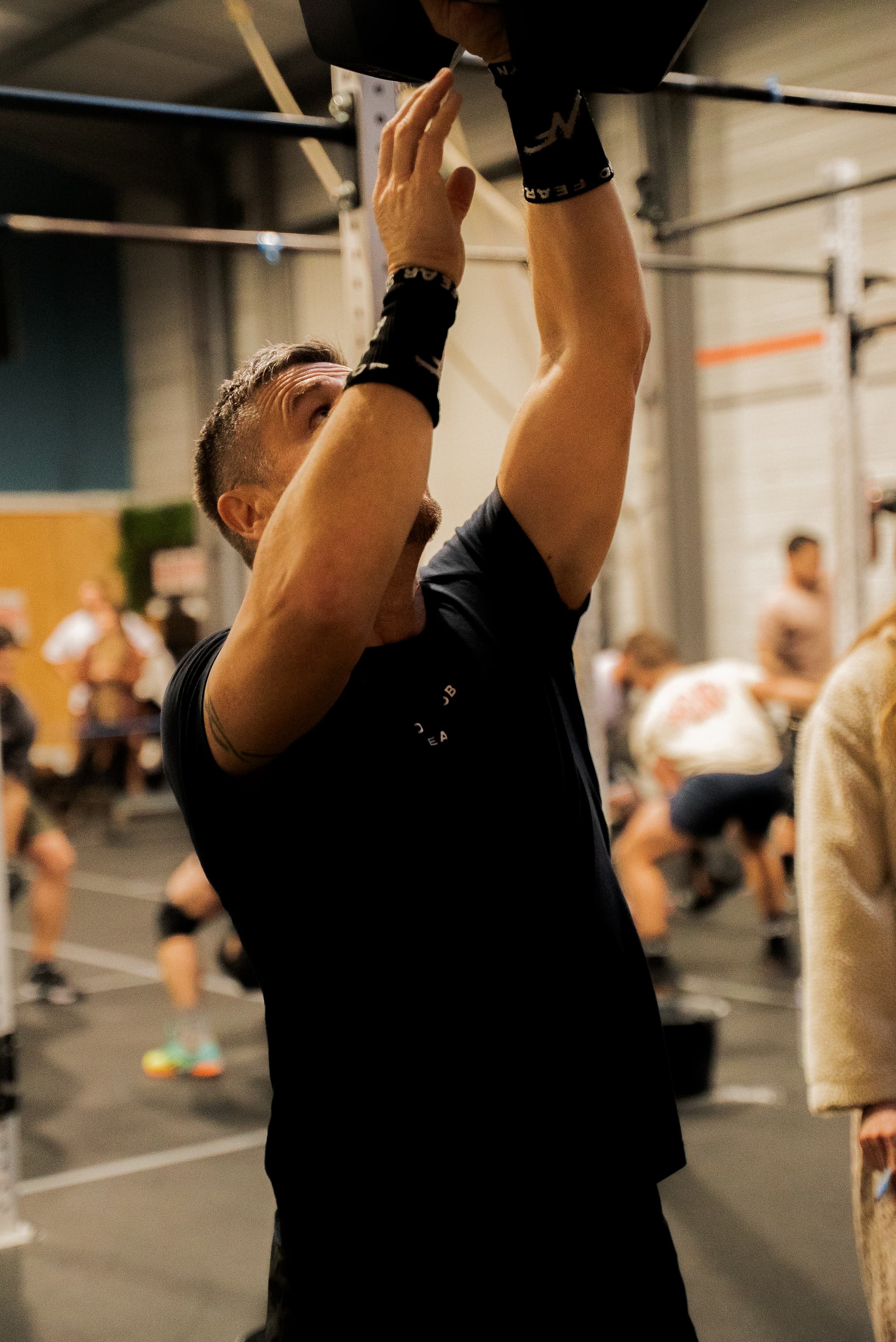 Jeune homme parlant dans un gymnase, entouré d'autres personnes, en train de faire de l'exercice, arrière-plan flou.