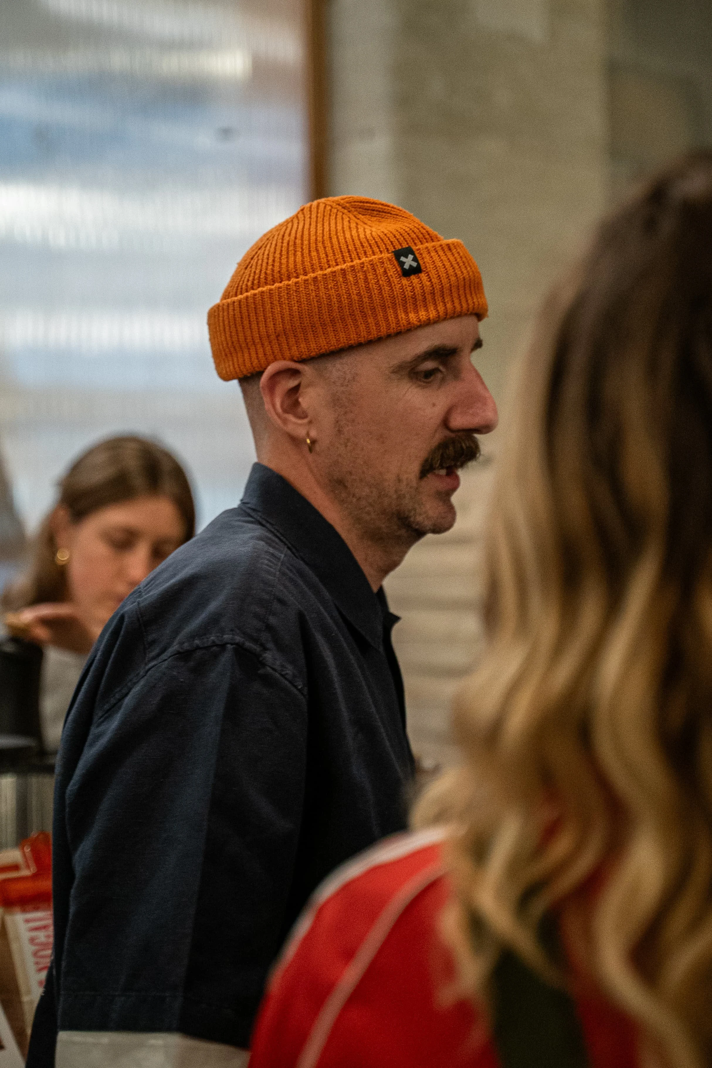 Un homme portant un bonnet orange se trouve dans une pièce, entouré de plusieurs autres personnes.