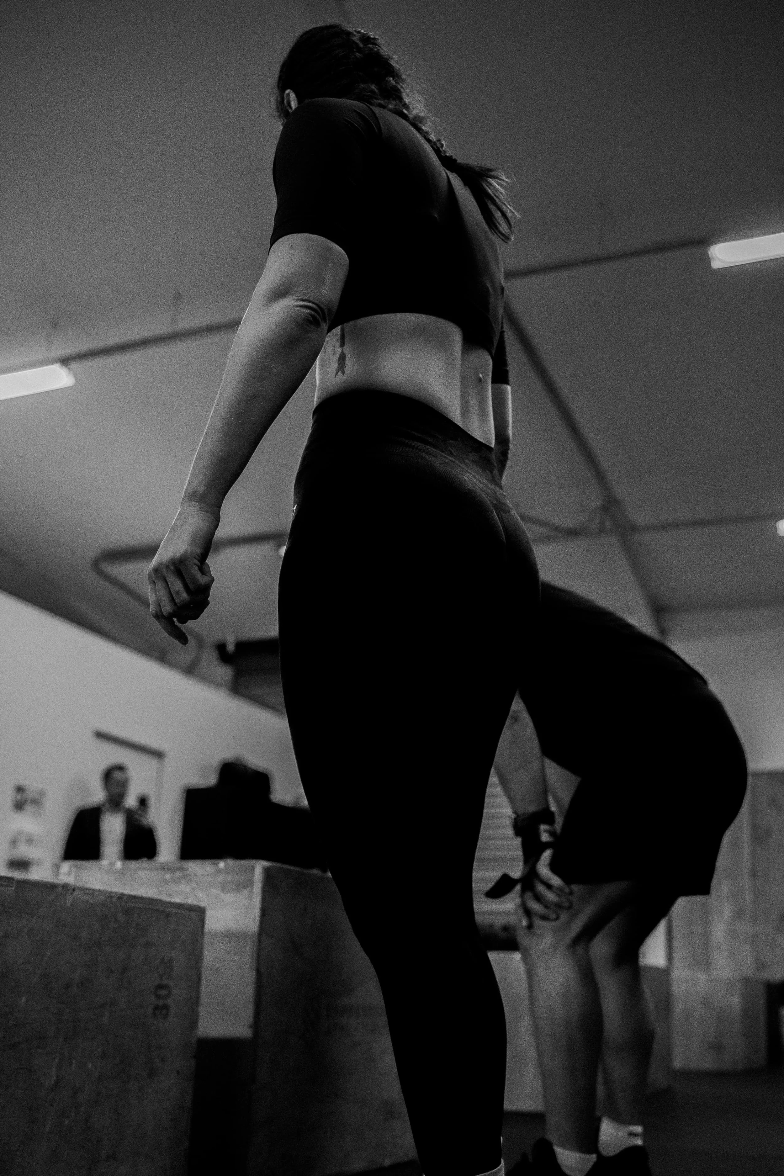 Femme en vêtements de sport, debout dans une salle de gym, vue de derrière, silhouette en noir et blanc.