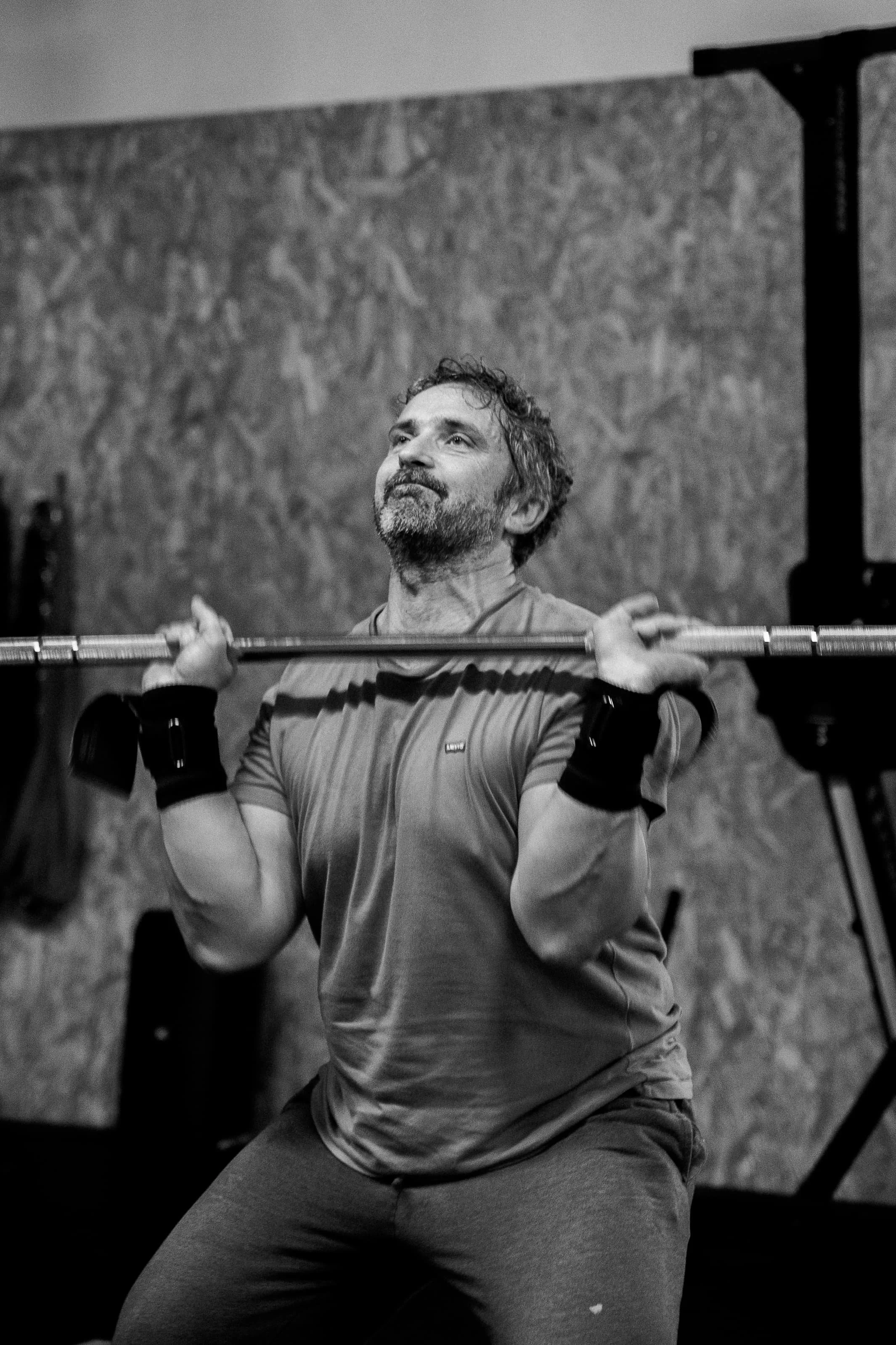 Une personne faisant un squat avec une barre lors d'entraînement en salle de sport, fond en bois, en noir et blanc.