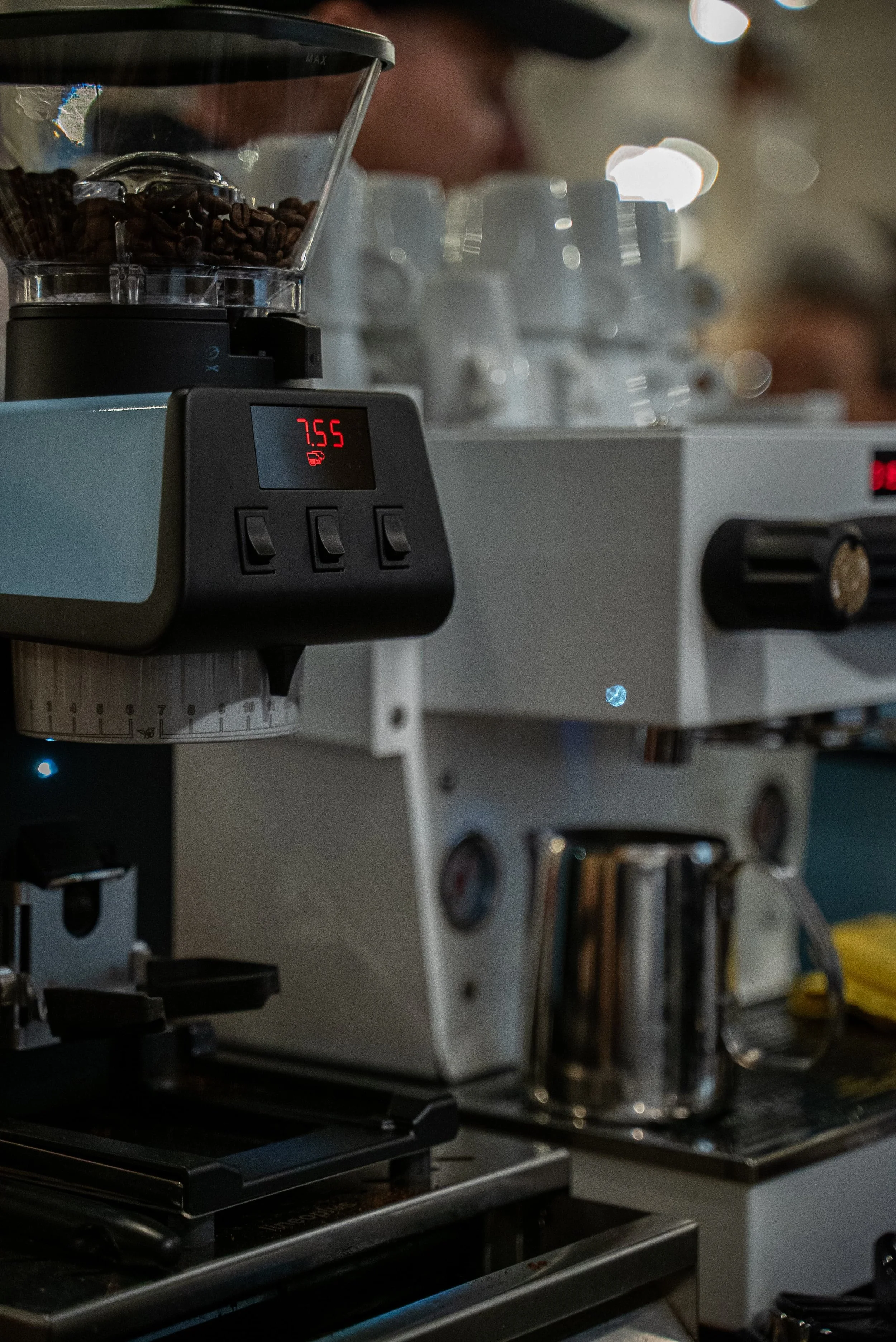Une machine à café avec des grains de café dans le moulin, un écran affichant 7.55, dans un environnement de café ou de cuisine.