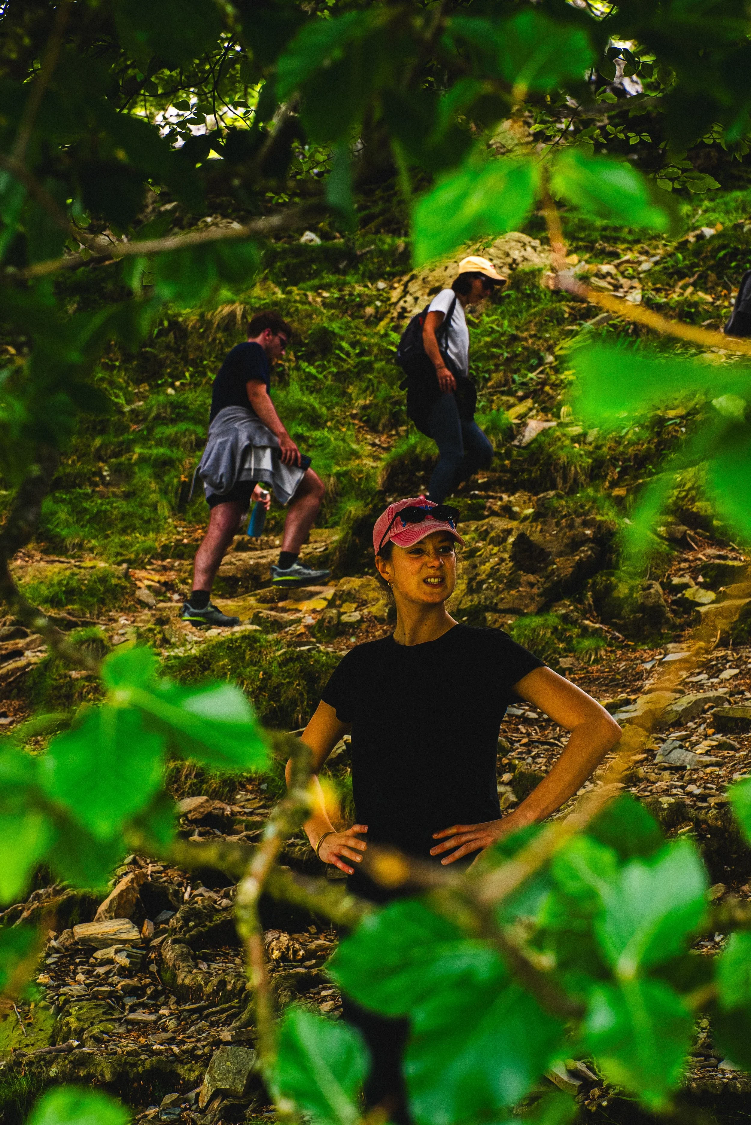 Trois personnes en randonnée dans une forêt, vue partielle à travers des feuilles vertes.