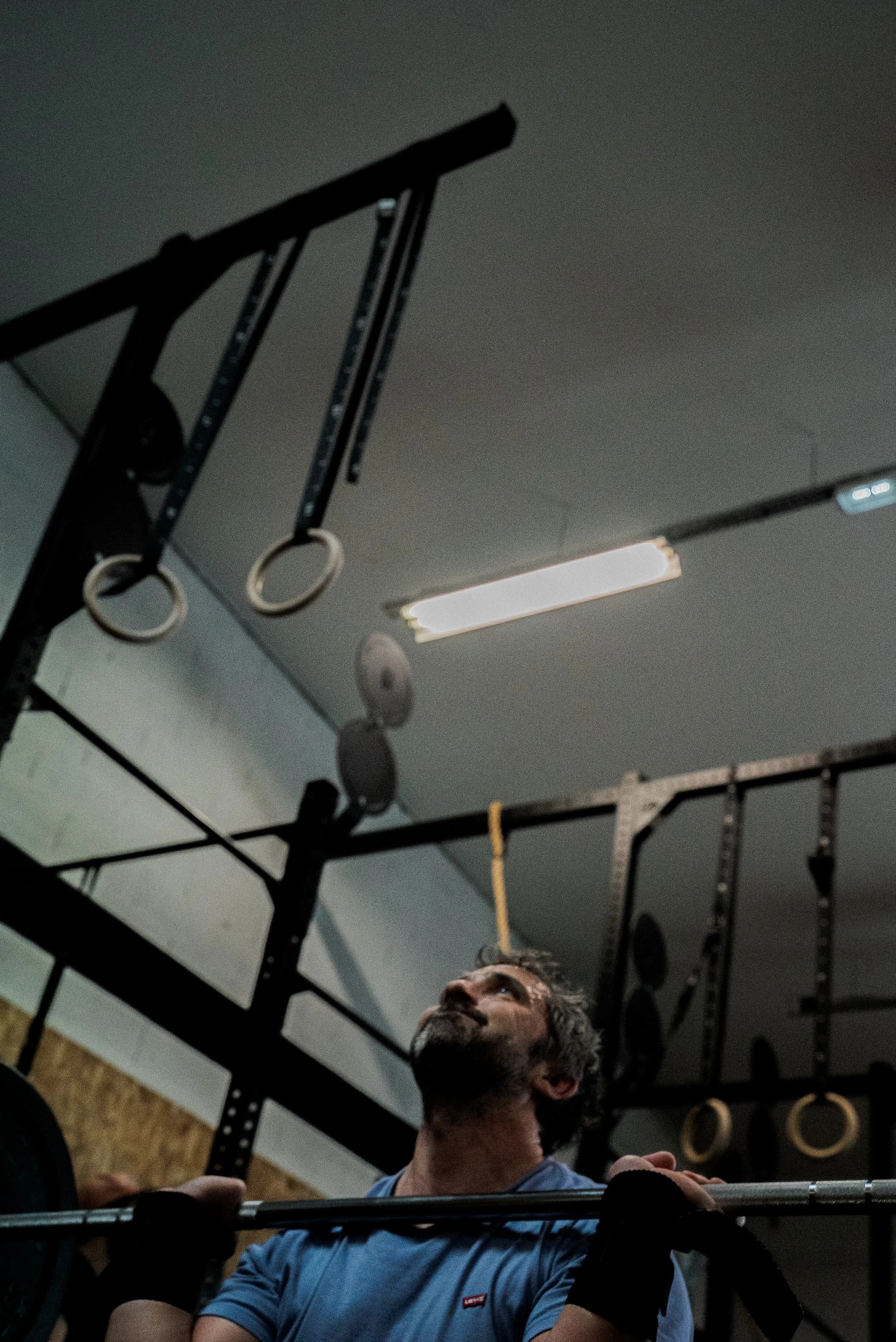 Un homme musclé effectuant un entraînement de musculation dans une salle de sport avec des anneaux de gymnastique suspendus au plafond.