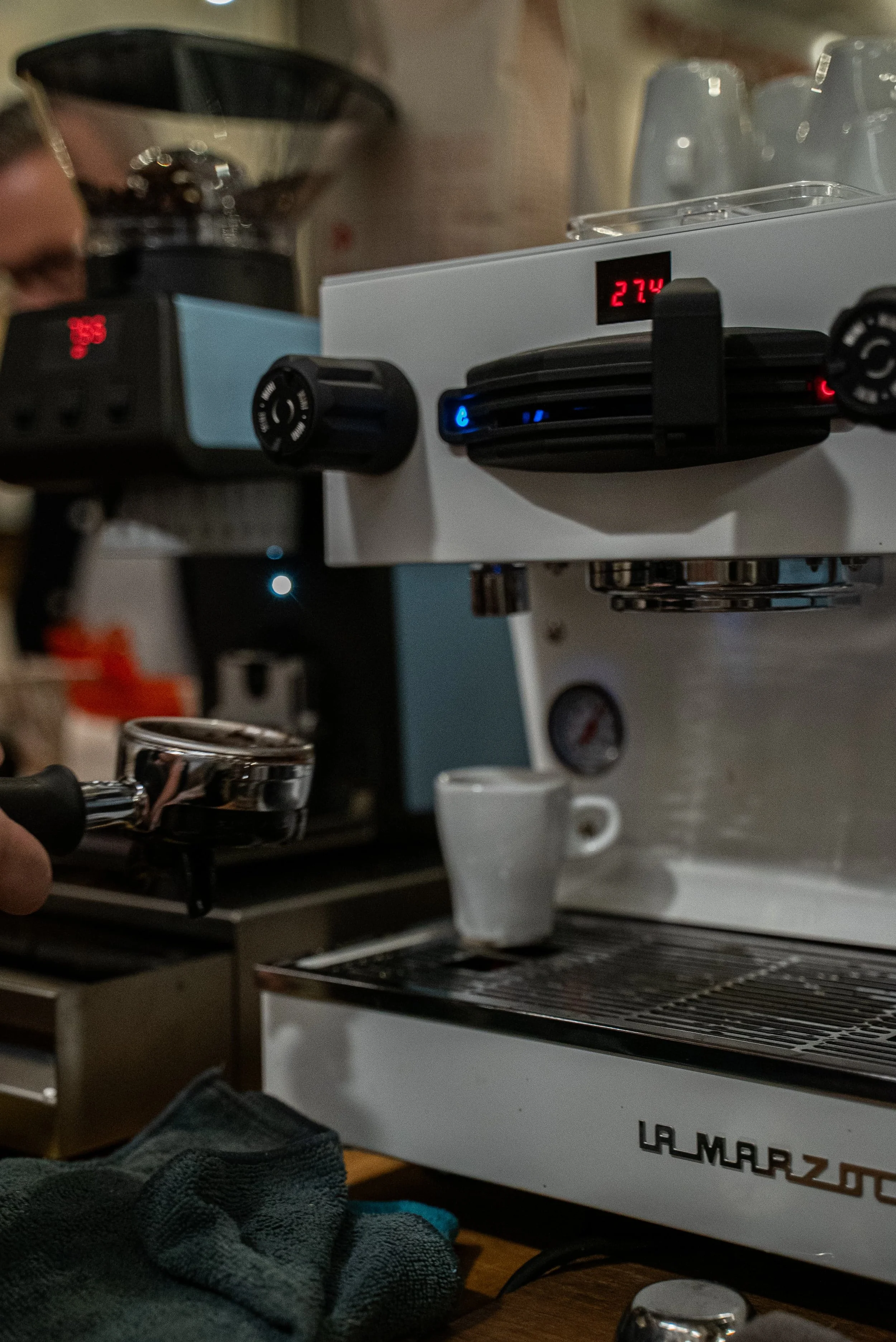 Une machine à café expresso en train d'extraire du café, avec une tasse palestinienne en dessous, dans une ambiance de cuisine ou de café.