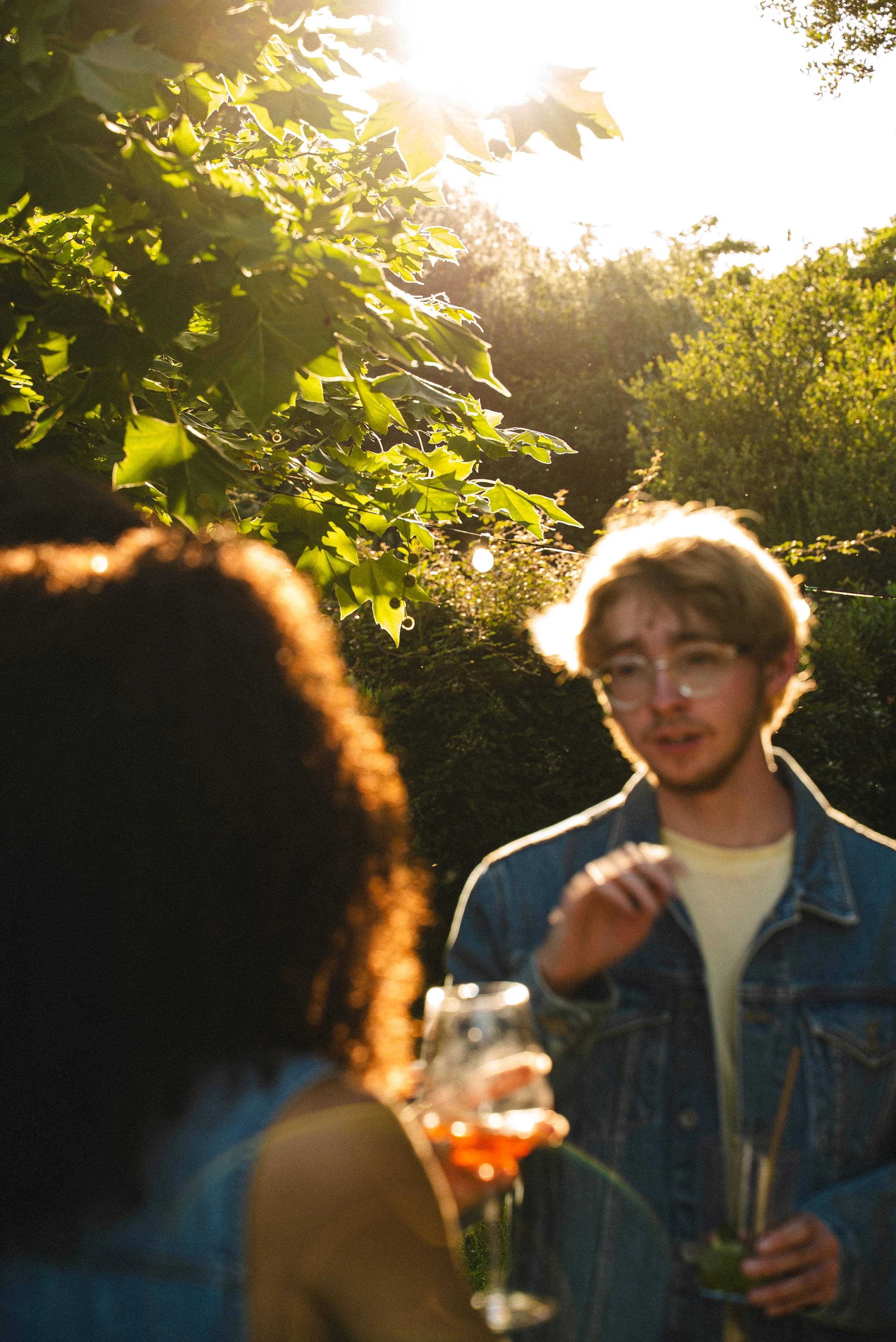 Groupe de personnes lors d'un rassemblement en plein air en soirée, avec soleil couchant, sirotant des boissons et engageant une conversation