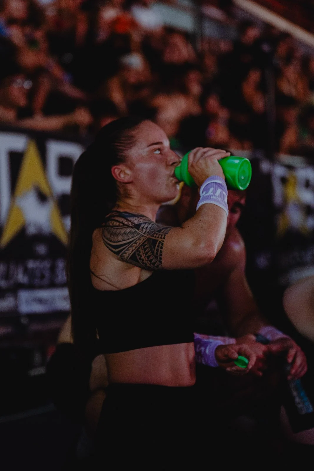 Athlète féminine s'hydratant avec bouteille verte lors d'un événement sportif bondé — photographe fitness Voar by Tim