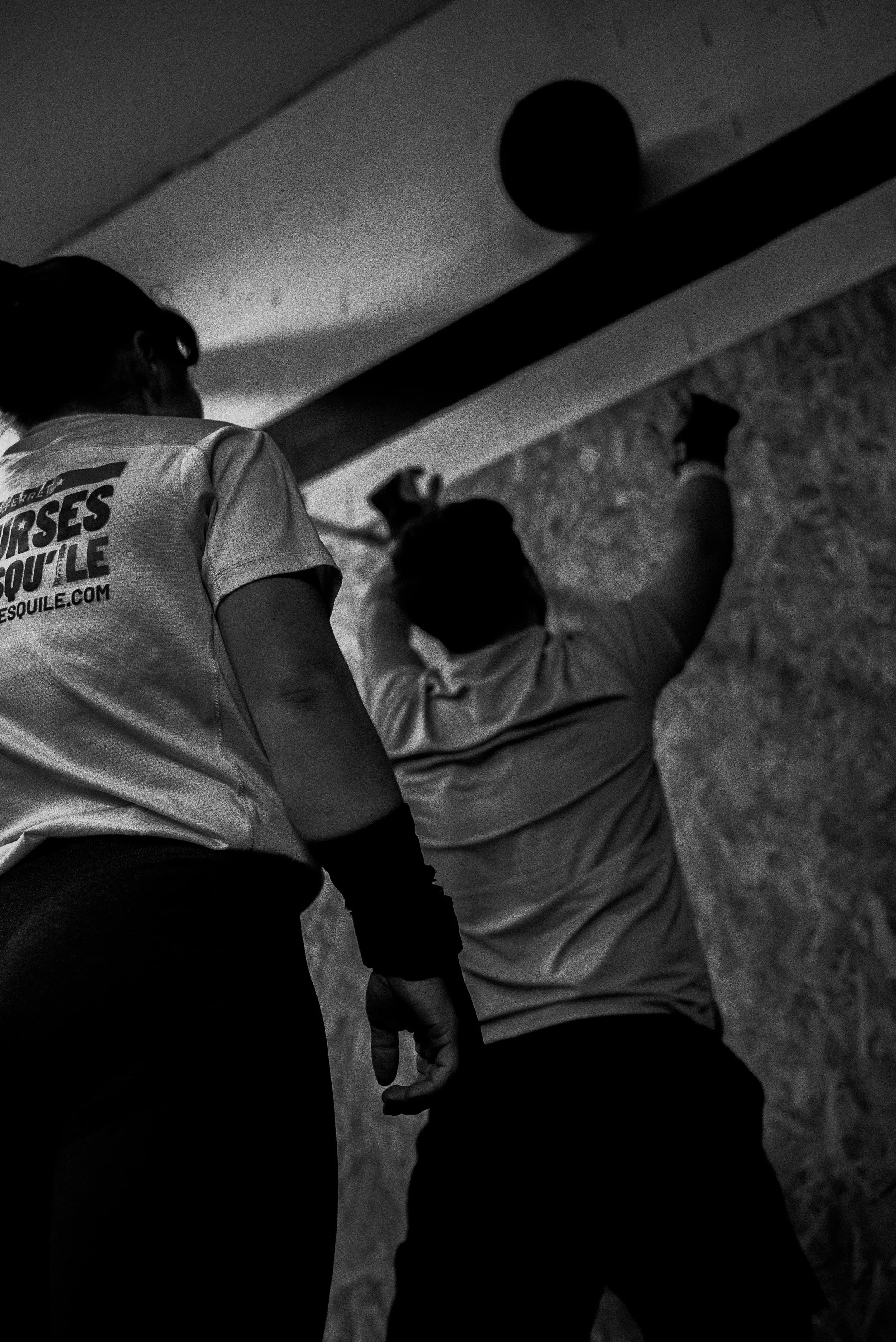 Deux personnes se tiennent par la main, vue de dos, dans un environnement intérieur avec un mur en pierre en arrière-plan.