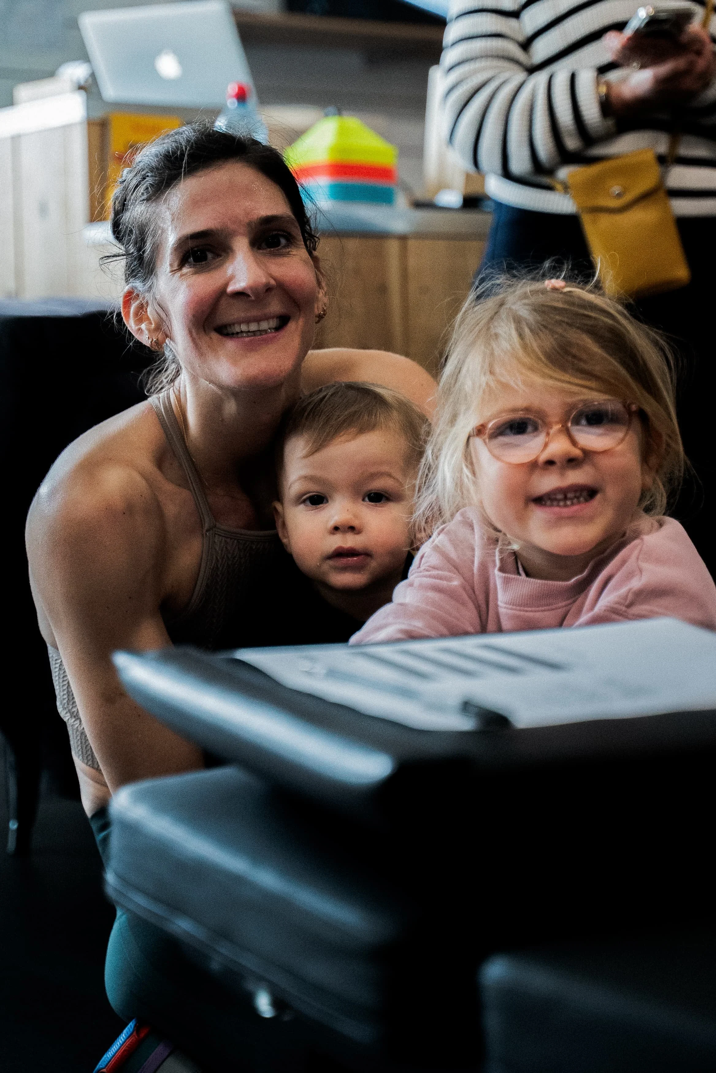 Une femme souriante avec deux enfants, un garçon et une fille, posant devant une machine à nourriture ou un appareil électronique, dans un intérieur.