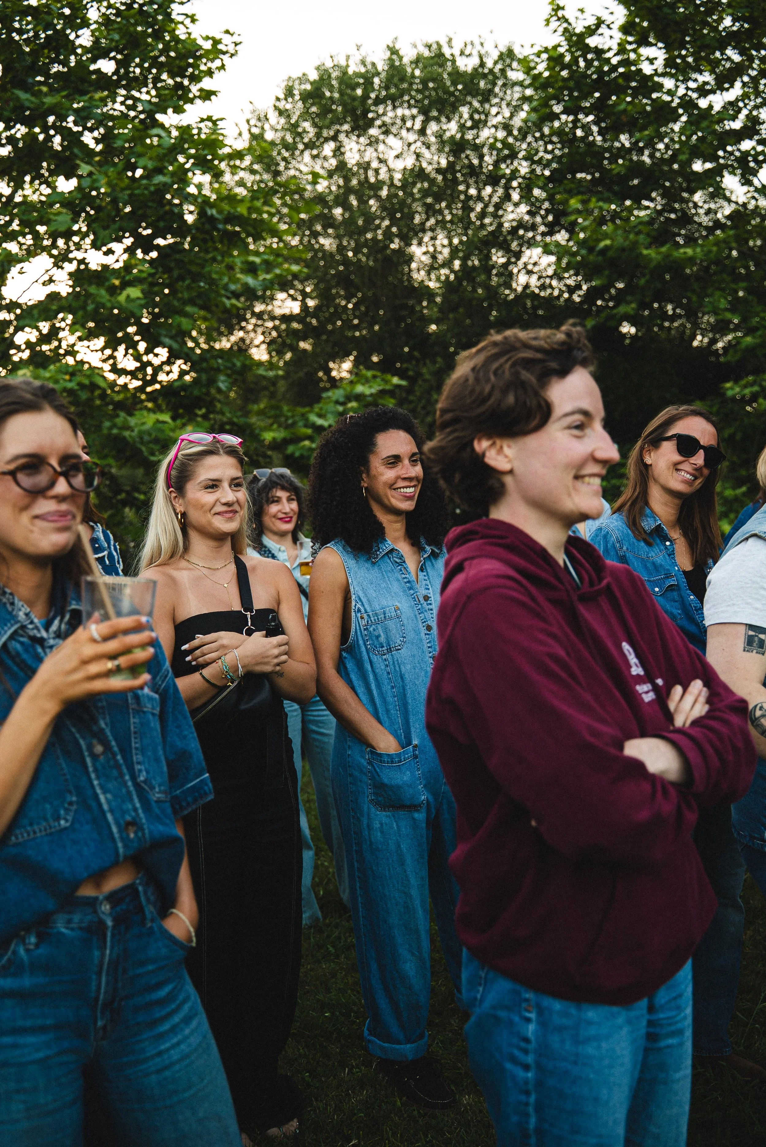 Groupe de personnes souriantes lors d'un rassemblement en plein air, entourées d'arbres, en fin d'après-midi ou en soirée.