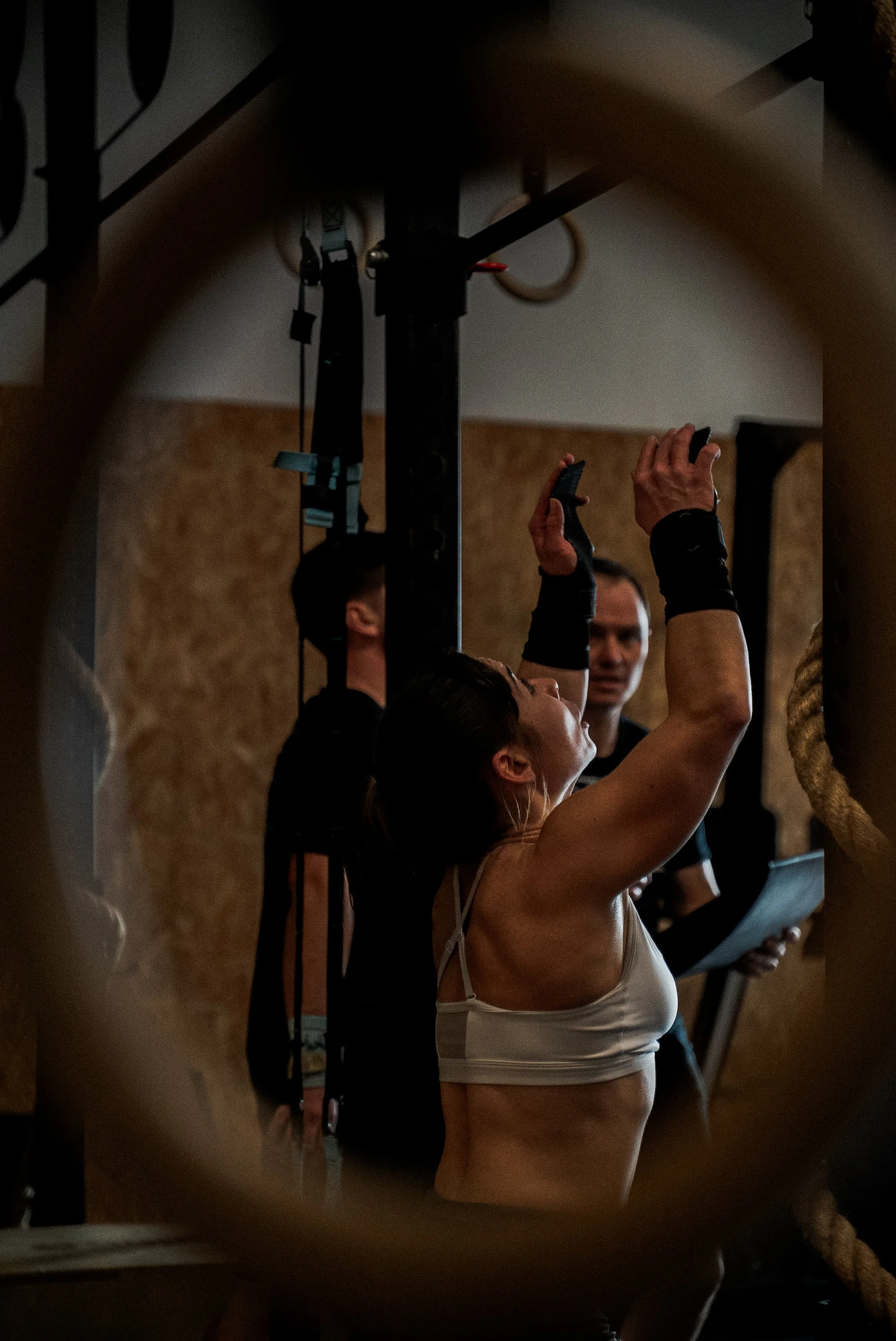 Une femme en tenue de sport ajuste quelque chose en haut lors d'une séance d'entraînement, avec un homme qui la regarde en arrière-plan.