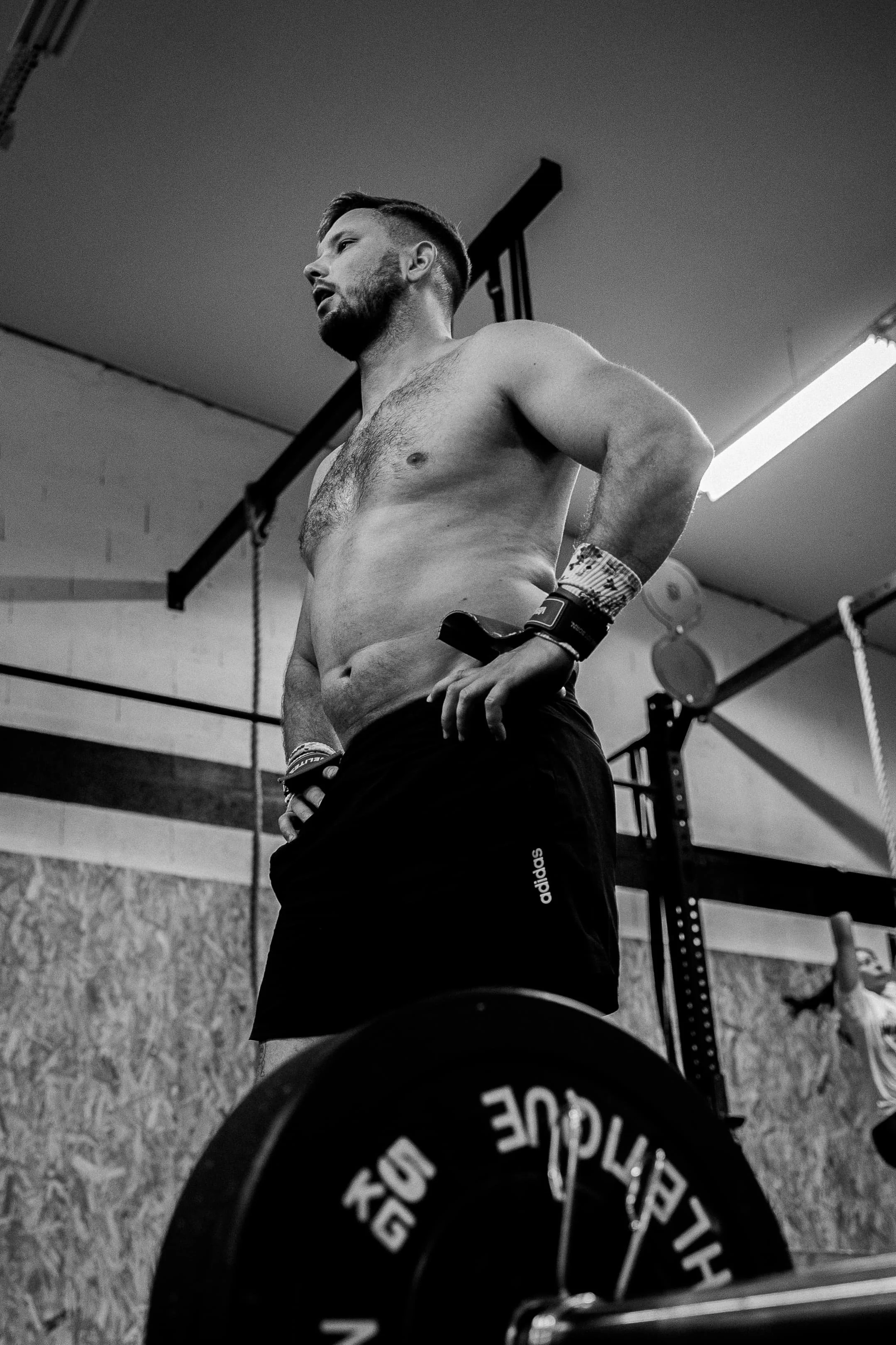 Un homme musclé, torse nu, portant un bracelet de sport, dans une salle de musculation, vue en contre-plongée.