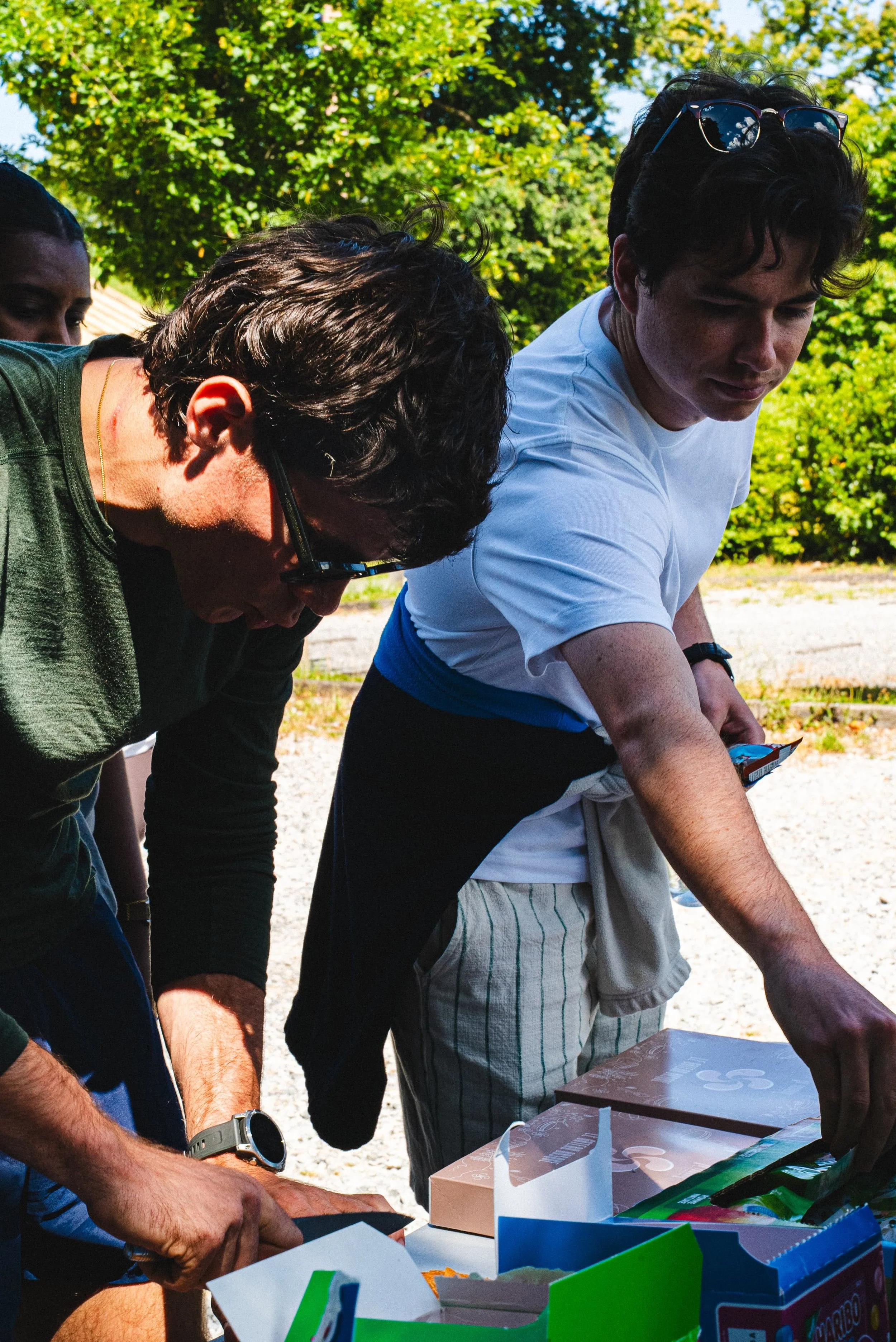 Groupe de personnes qui assemblent ou jouent à un jeu de société sur une table en plein air, avec un arrière-plan de feuillage vert.