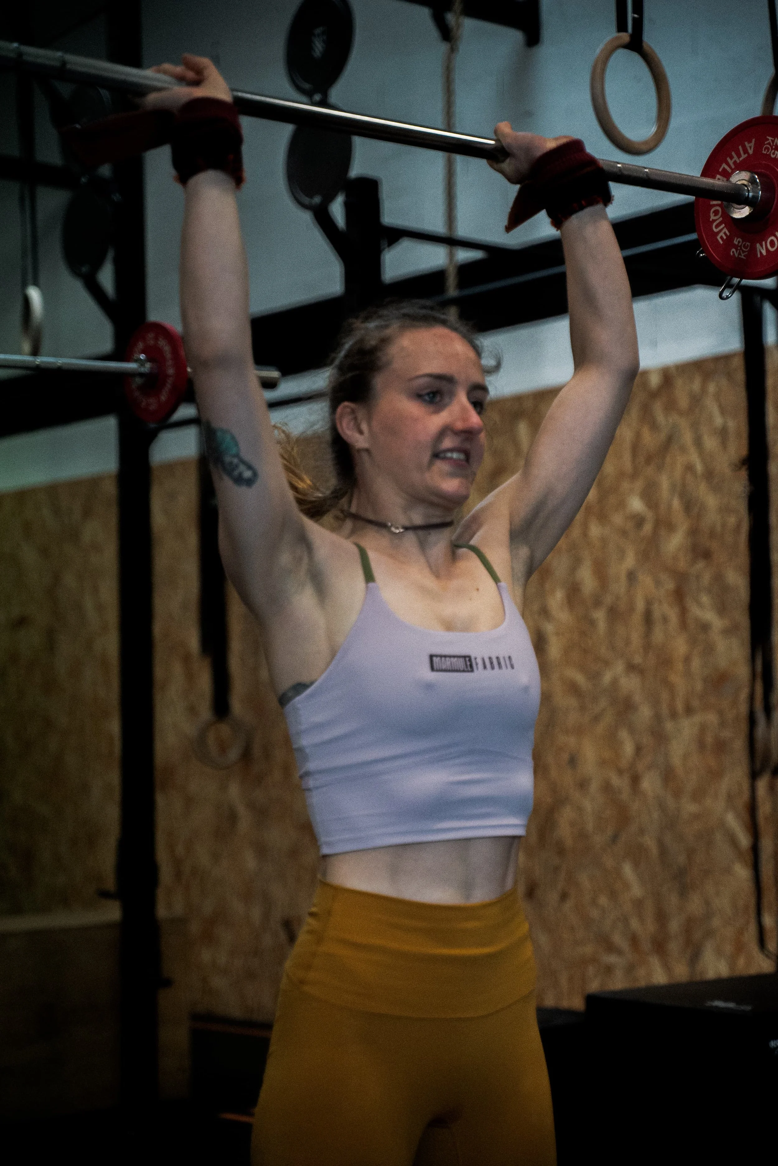 Une femme en vêtements de sport soulève une barre avec des disques de poids dans une salle de musculation.