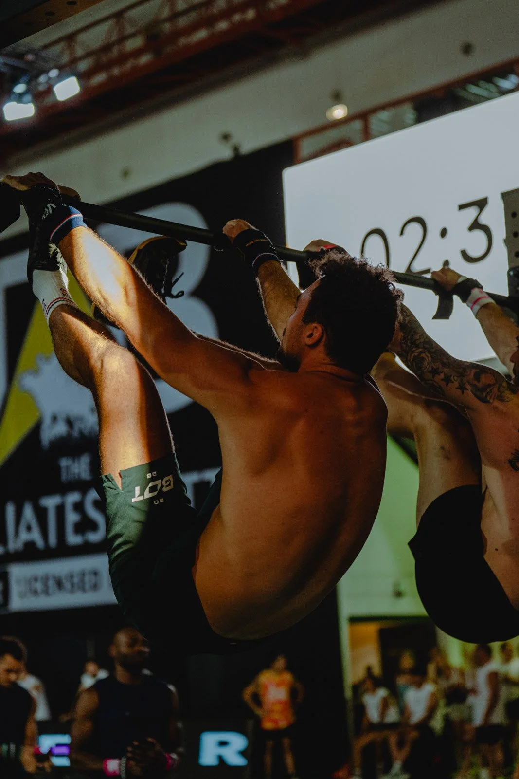 Homme suspendu à une barre lors d'une compétition de CrossFit avec public en Nouvelle-Aquitaine — photographe CrossFit Voar by Tim
