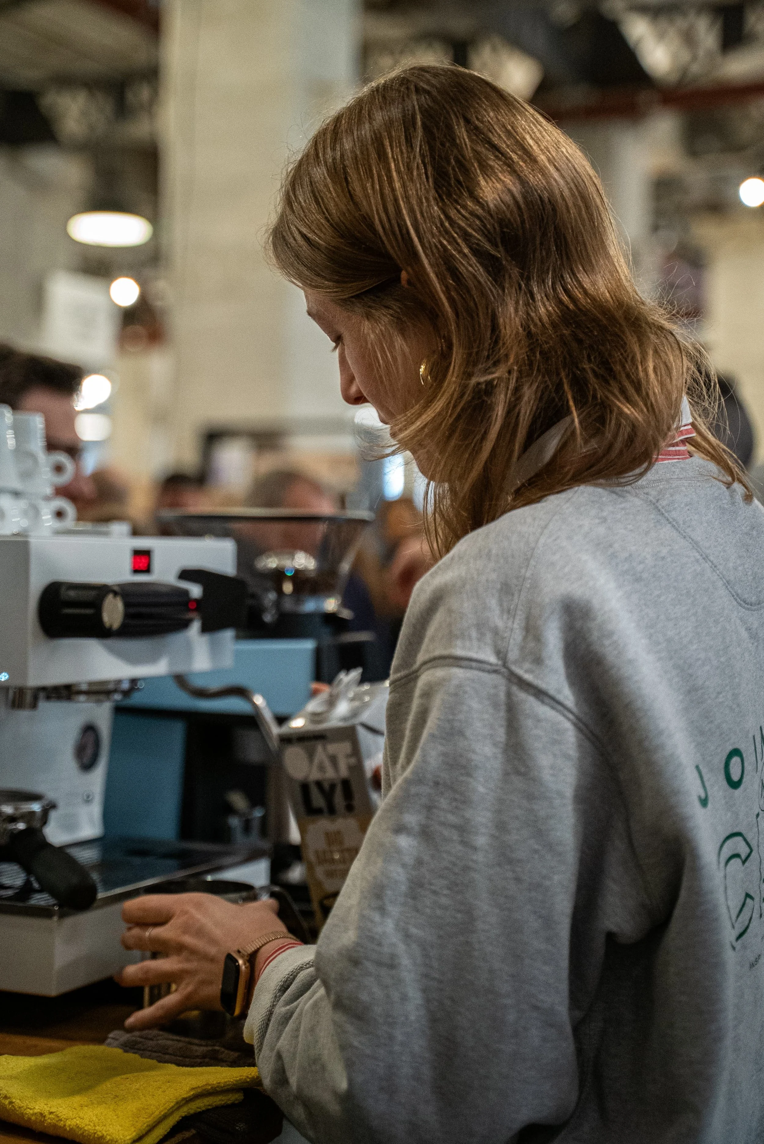 Une femme est à la machine à café dans un café ou un restaurant en intérieur, concentrée sur sa tâche.
