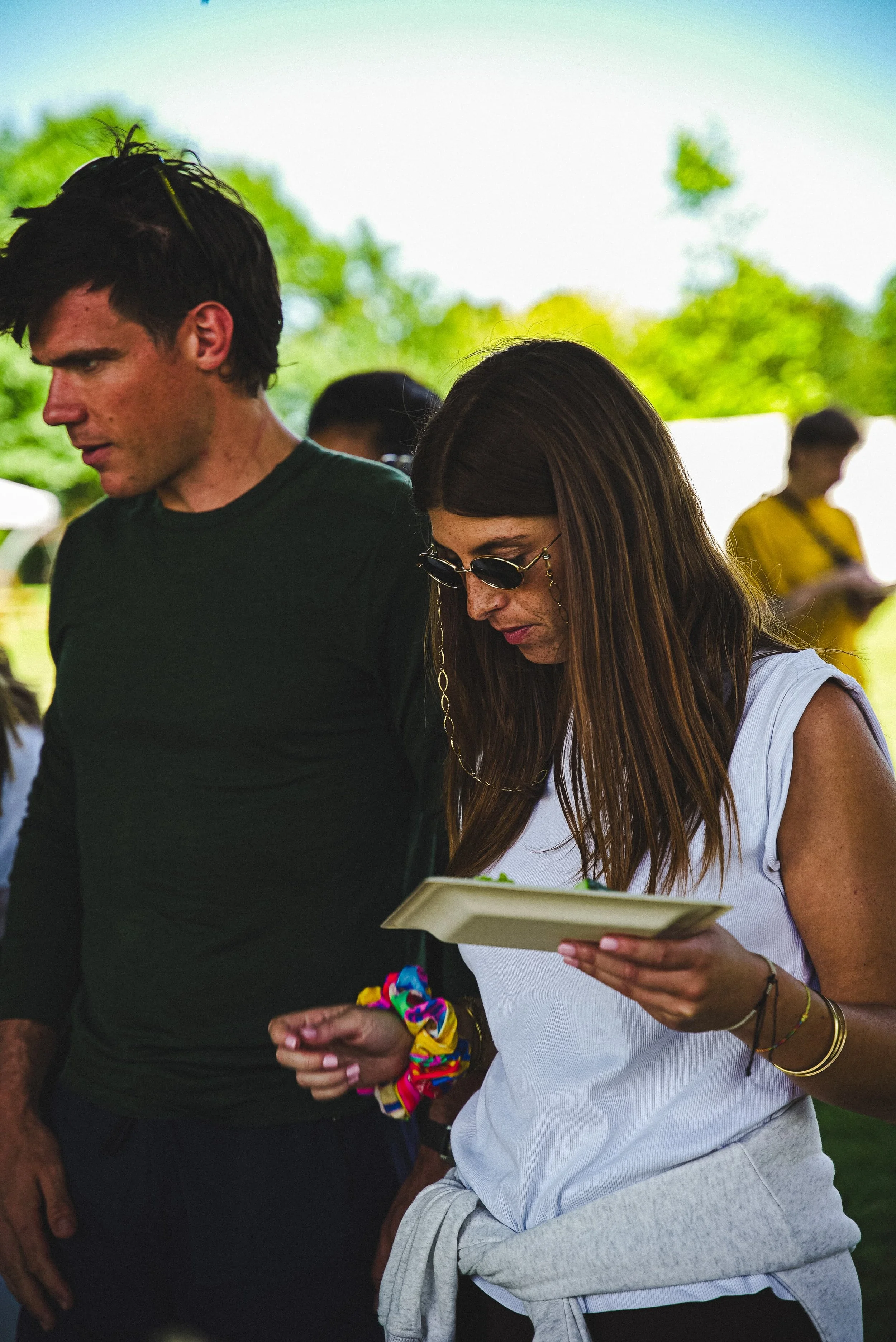 Deux jeunes femmes regardent un téléphone portable et une tablette lors d'un événement en plein air, avec un arrière-plan herbeux et quelques autres personnes.