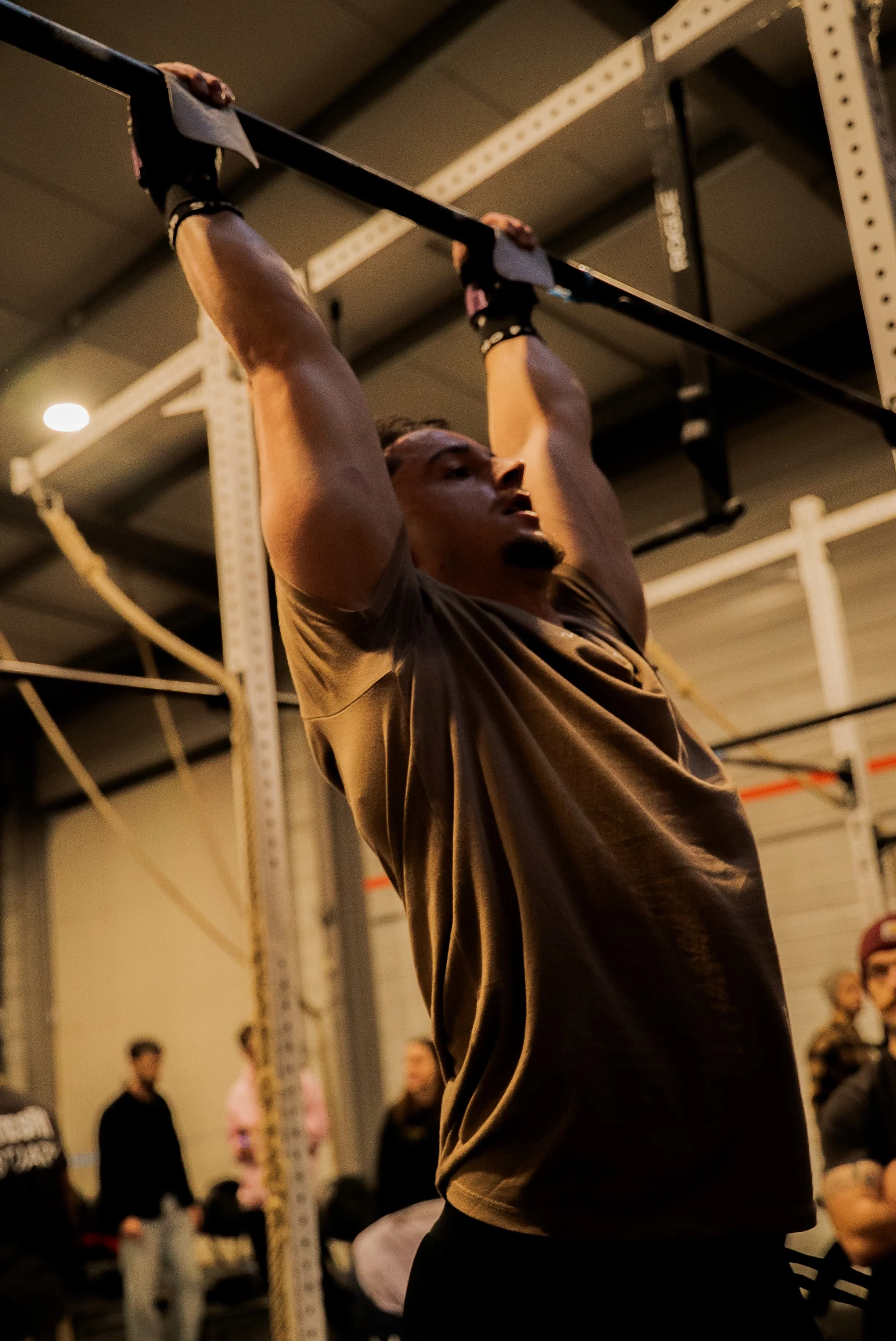 Une personne soulève une barre lors d'un entraînement de musculation en intérieur, avec d'autres personnes en arrière-plan.