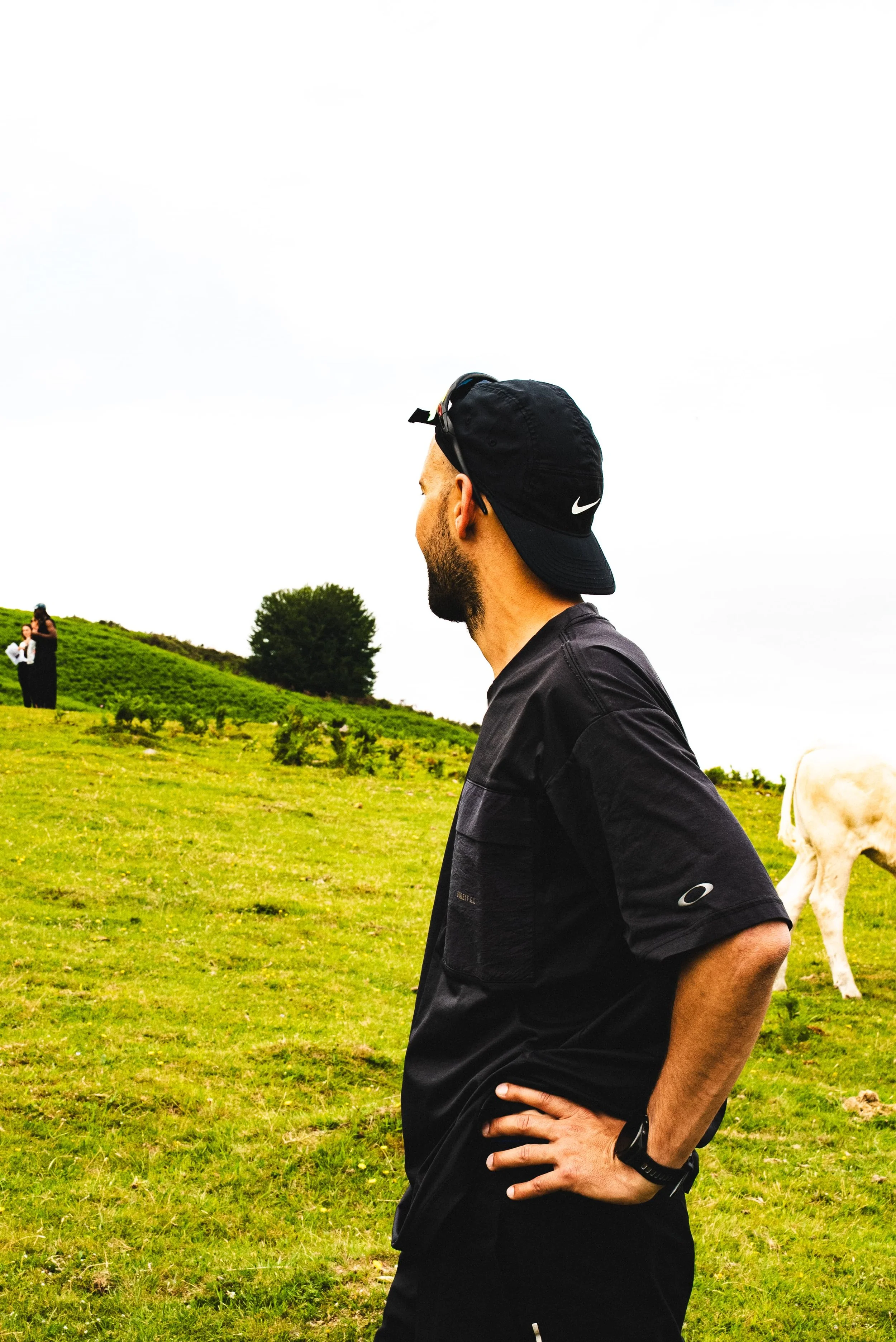 Homme en tenu de sport avec une casquette Nike, posant dans un champ verts avec un cheval et deux femmes en arrière-plan.
