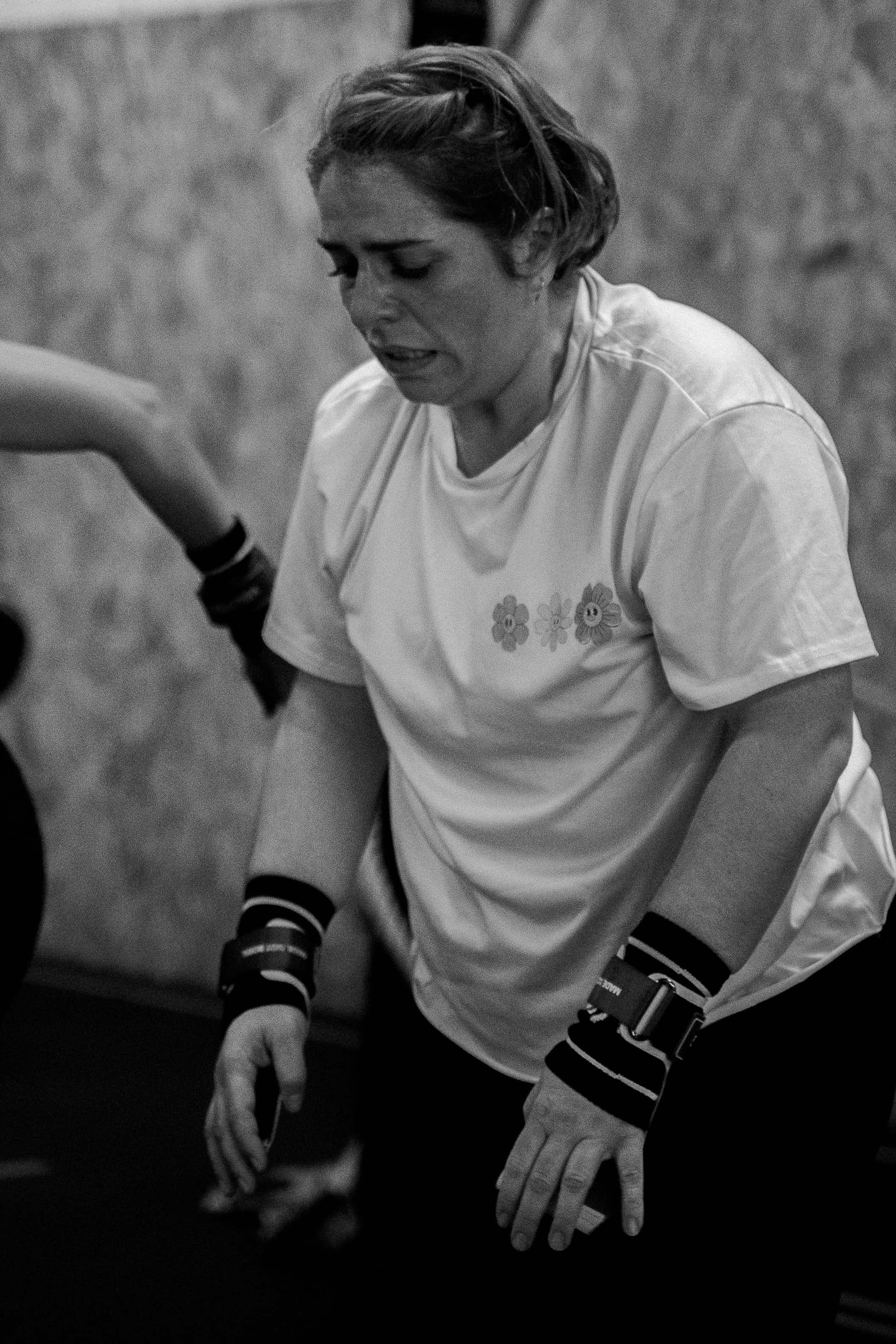 Jeune femme portant un maillot blanc avec des motifs de fleurs souriant et jouant au basket-ball, avec des gants, des genouillères et un gant de sport.