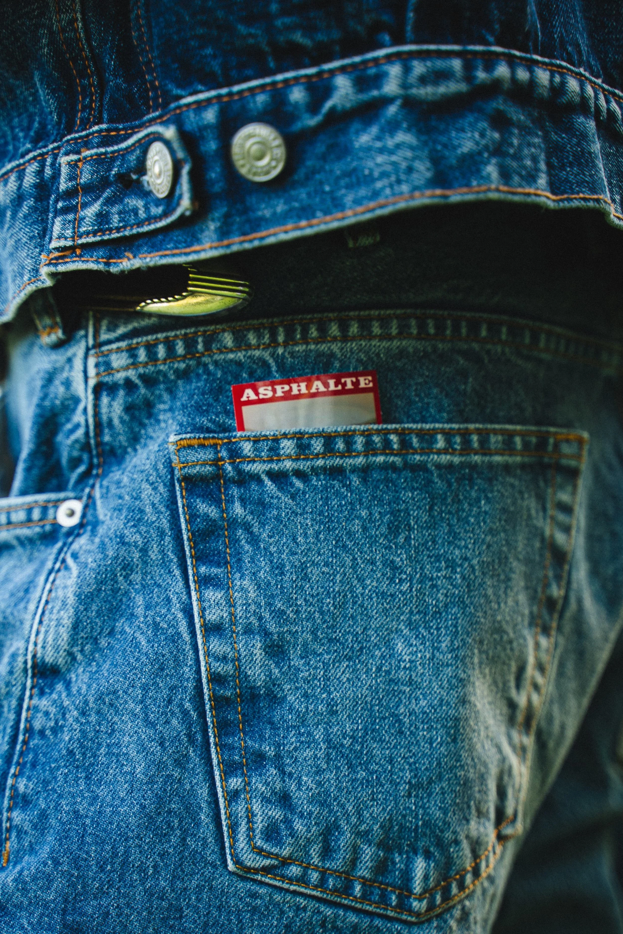 Une poche de jean avec une étiquette rouge portant le mot 'ASPHALTE' et un bouton métallique.