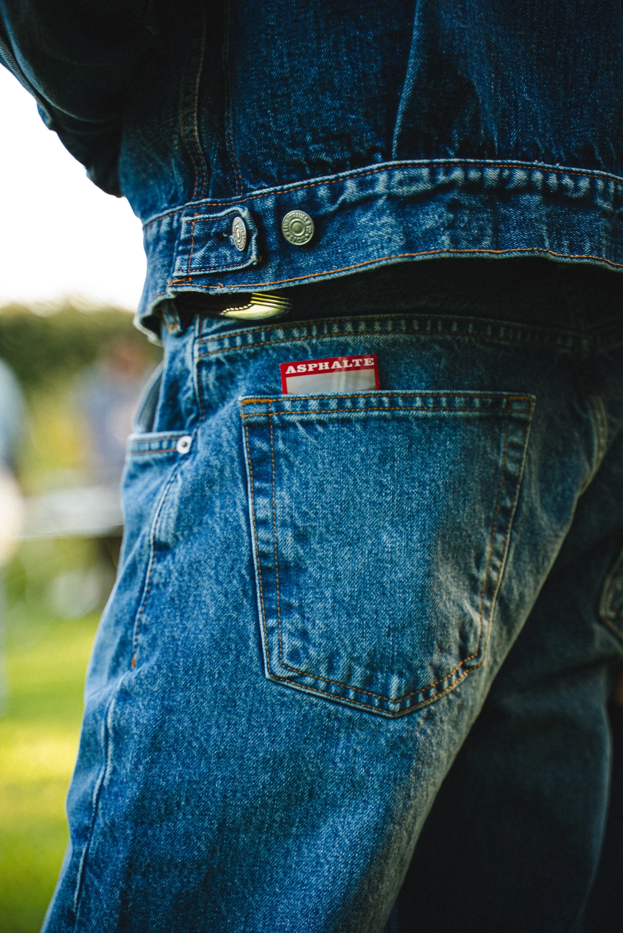 Un jean skinny bleu foncé avec une étiquette rouge où est écrit 'ASPHALTE' visible dans la poche arrière.
