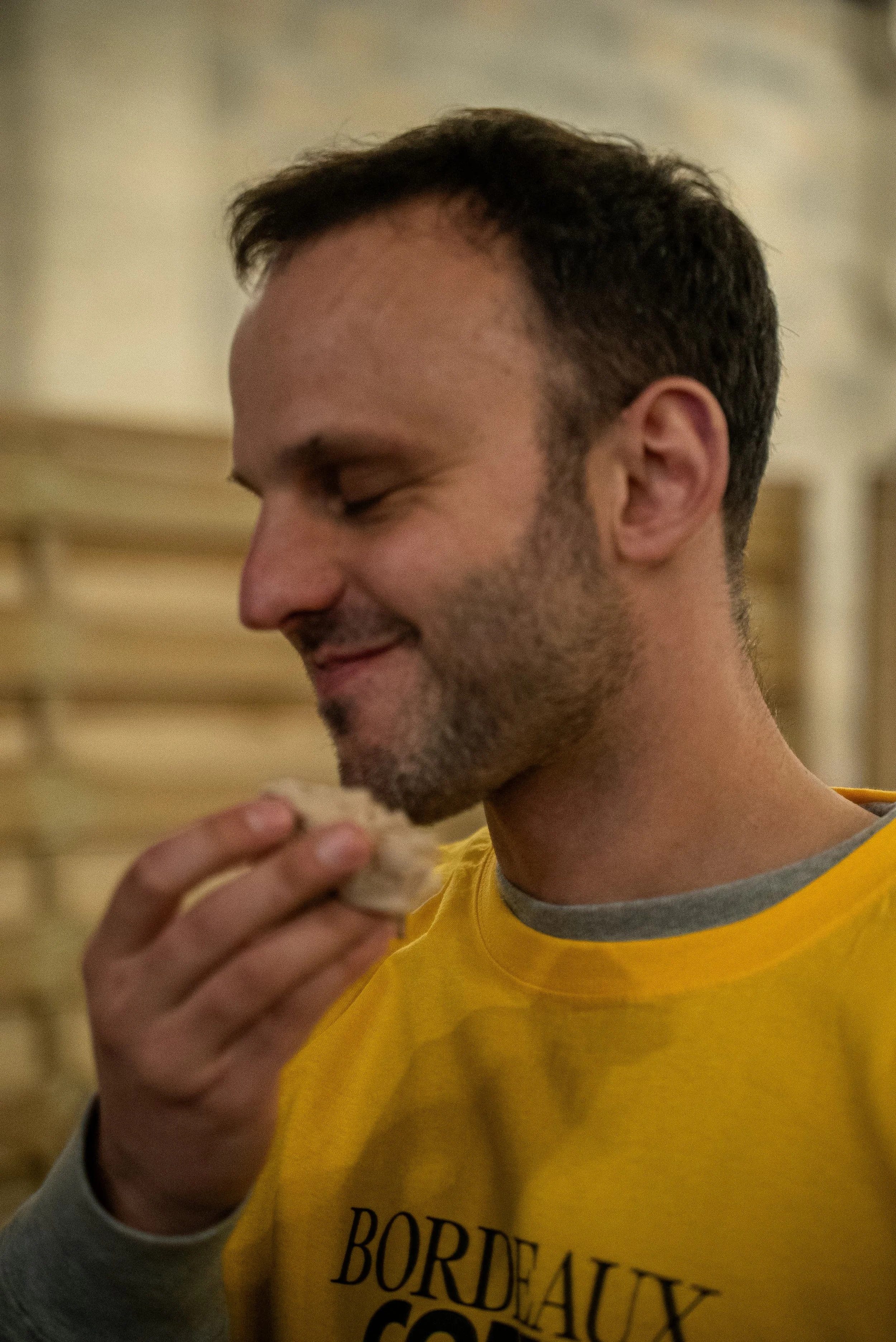 Un homme avec une barbe, portant un t-shirt jaune avec l'inscription 'BORDEAUX', qui tient une chauve-souris en main.
