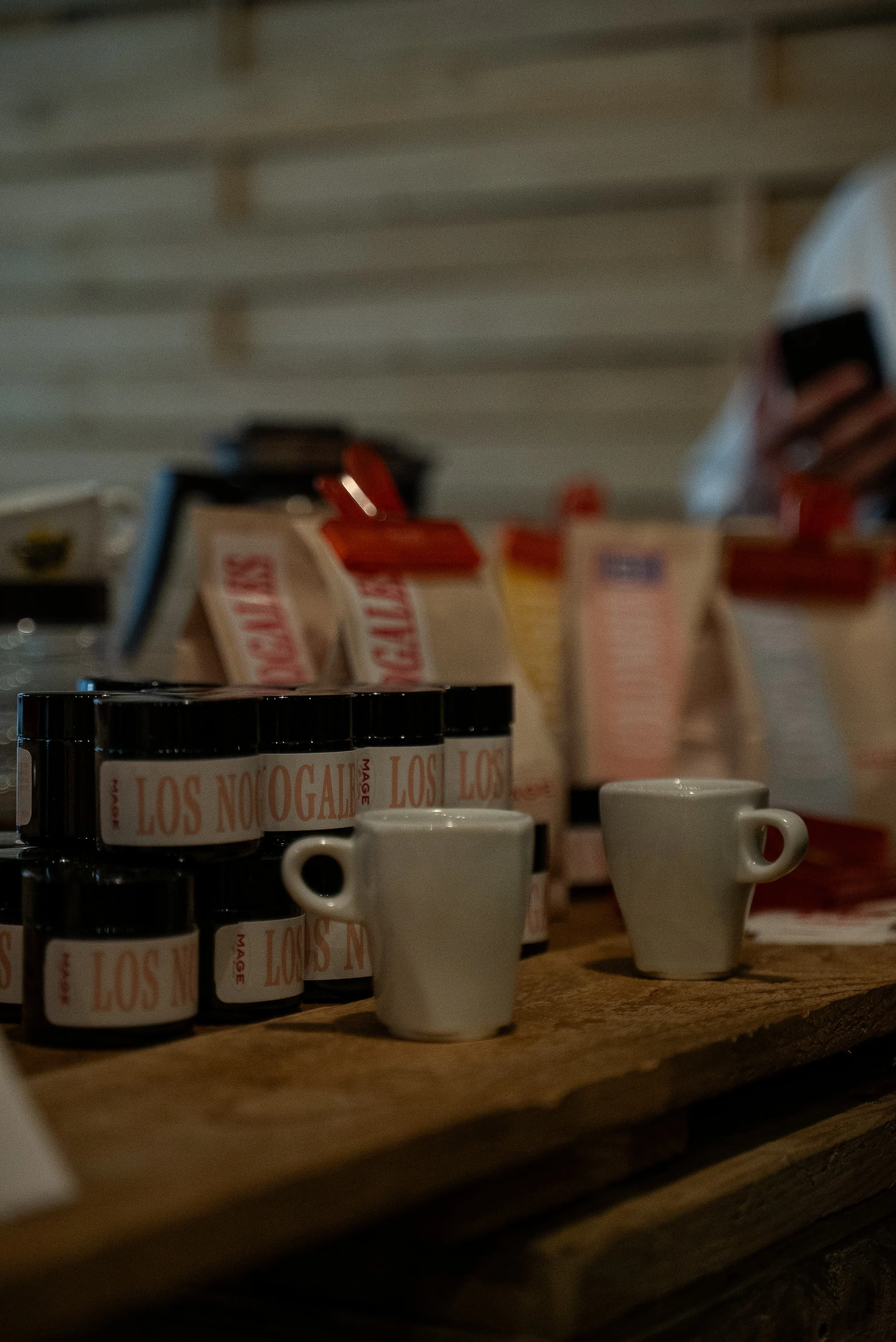 Tasses en céramique blanches avec des logos 'LOS ANGELES MAGIE', disposées sur une étagère en bois, avec des paquets de café en arrière-plan.