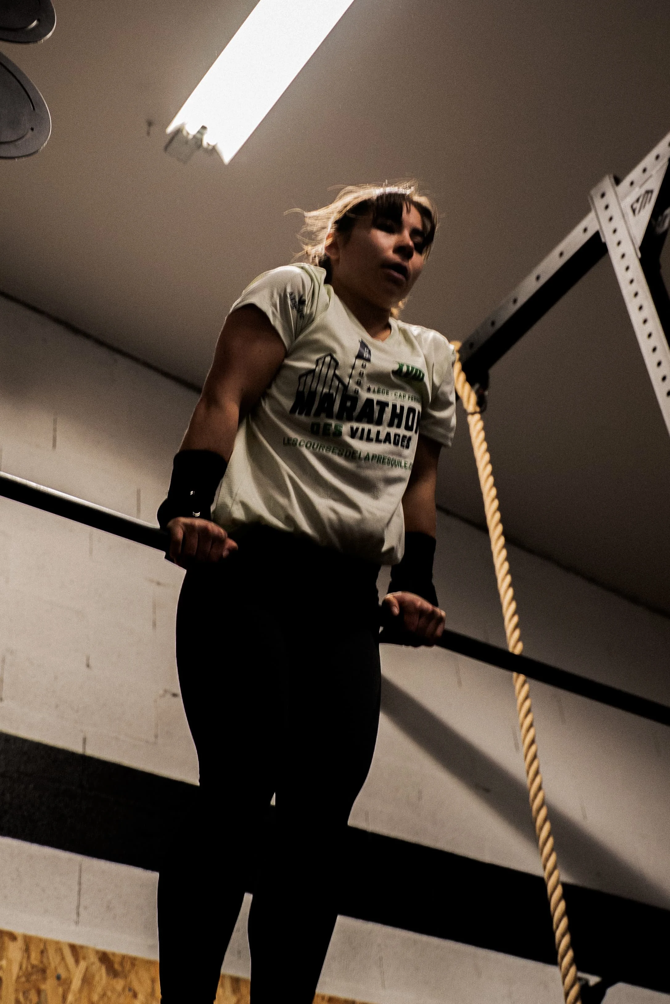 Une femme en tenue de sport, effectuant un entraînement de musculation, accroché à une barre de traction dans une salle de sport, avec une corde d'escalade à côté.