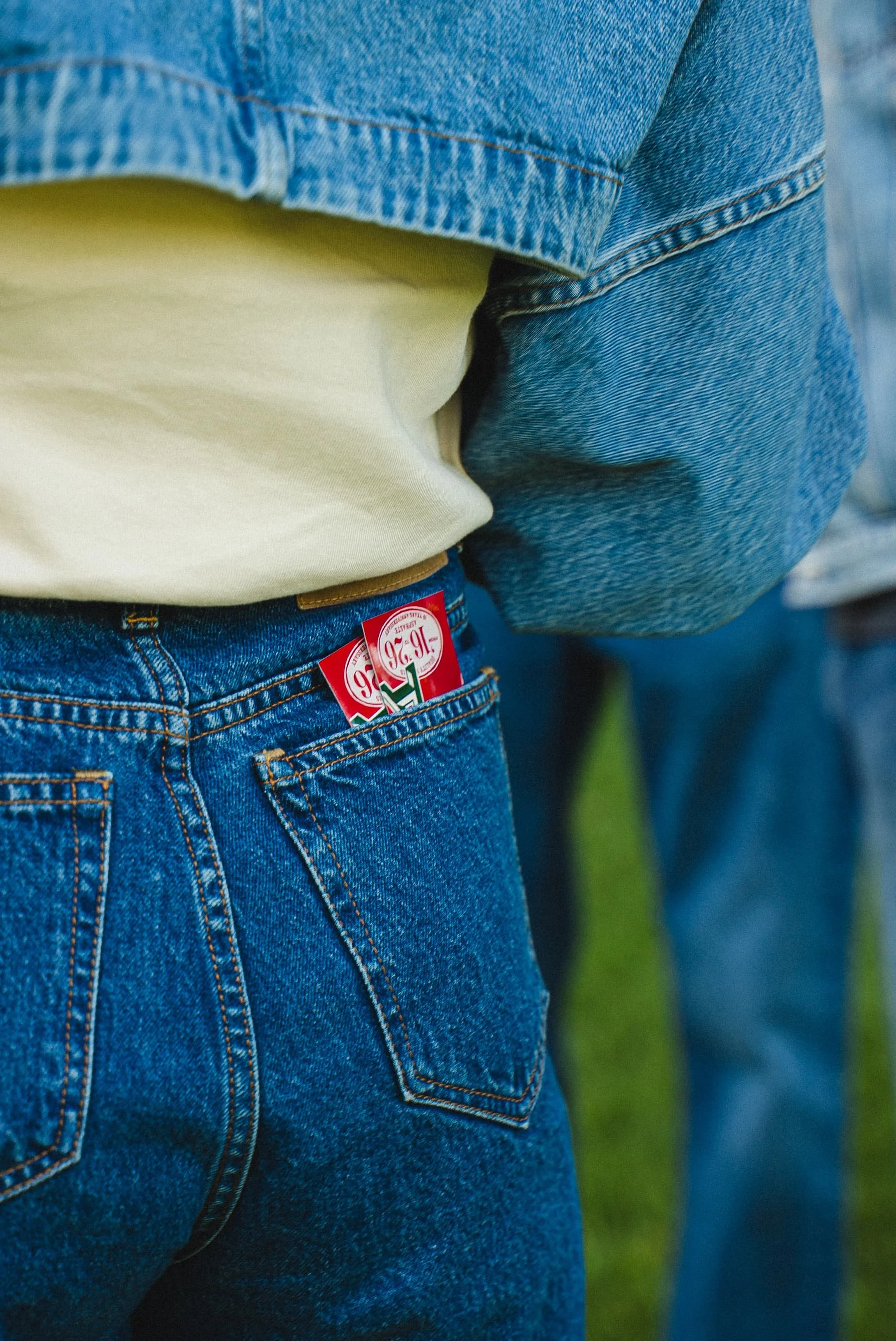 Photo en gros plan du dos d'une personne portant un jean bleu et un t-shirt beige, avec une étiquette rouge sur la poche arrière du jean.