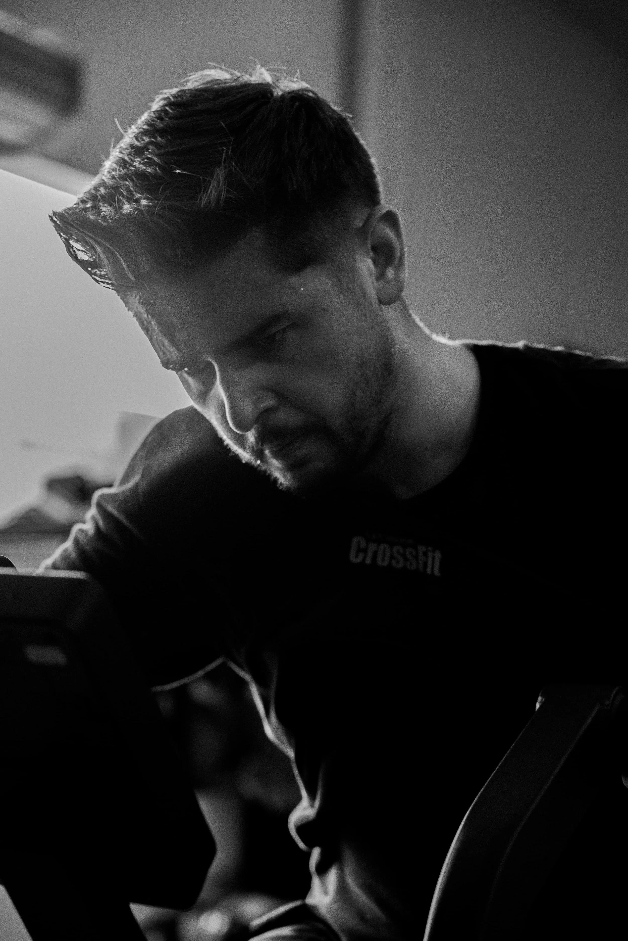 Un homme avec des cheveux courts et une barbe, portant un t-shirt noir avec le mot 'CrossFit' écrit dessus, joue de la guitare