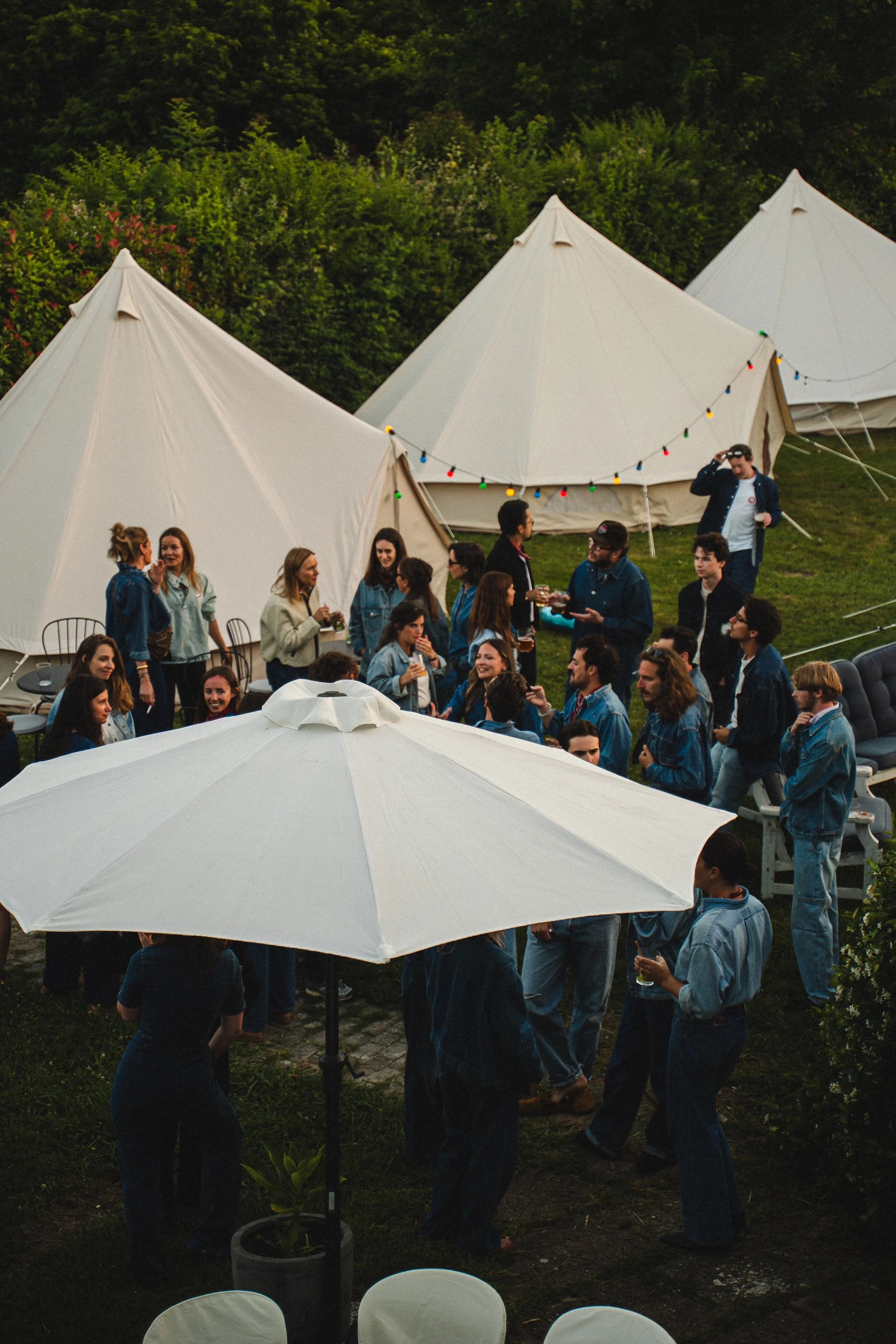 Groupe de personnes en extérieur lors d'une fête ou d'un rassemblement, avec tentes blanches et décoration lumineuse.