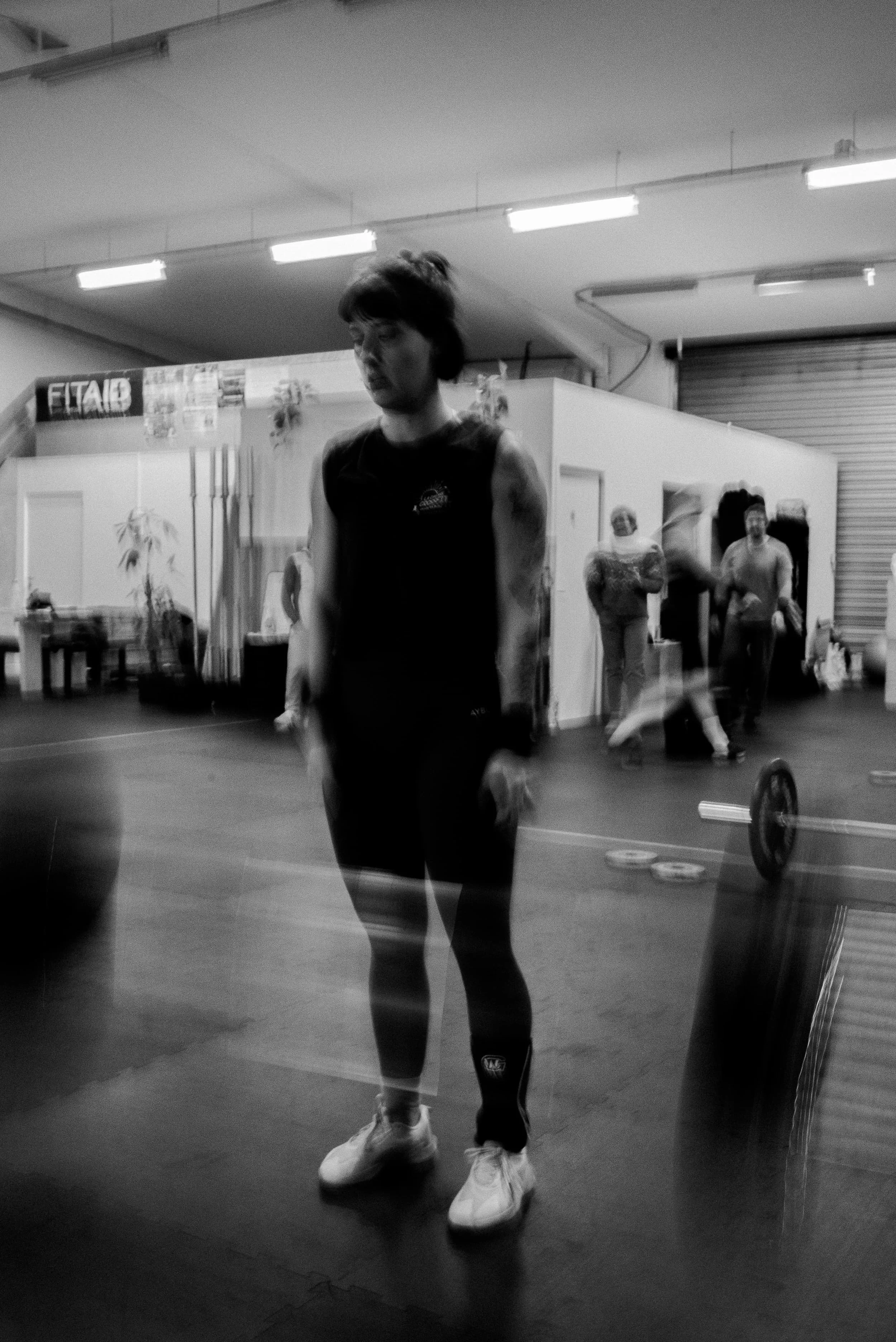 Une femme en vêtements de sport, portant des chaussures de sport blanches, se trouve dans une salle de sport ou de fitness.