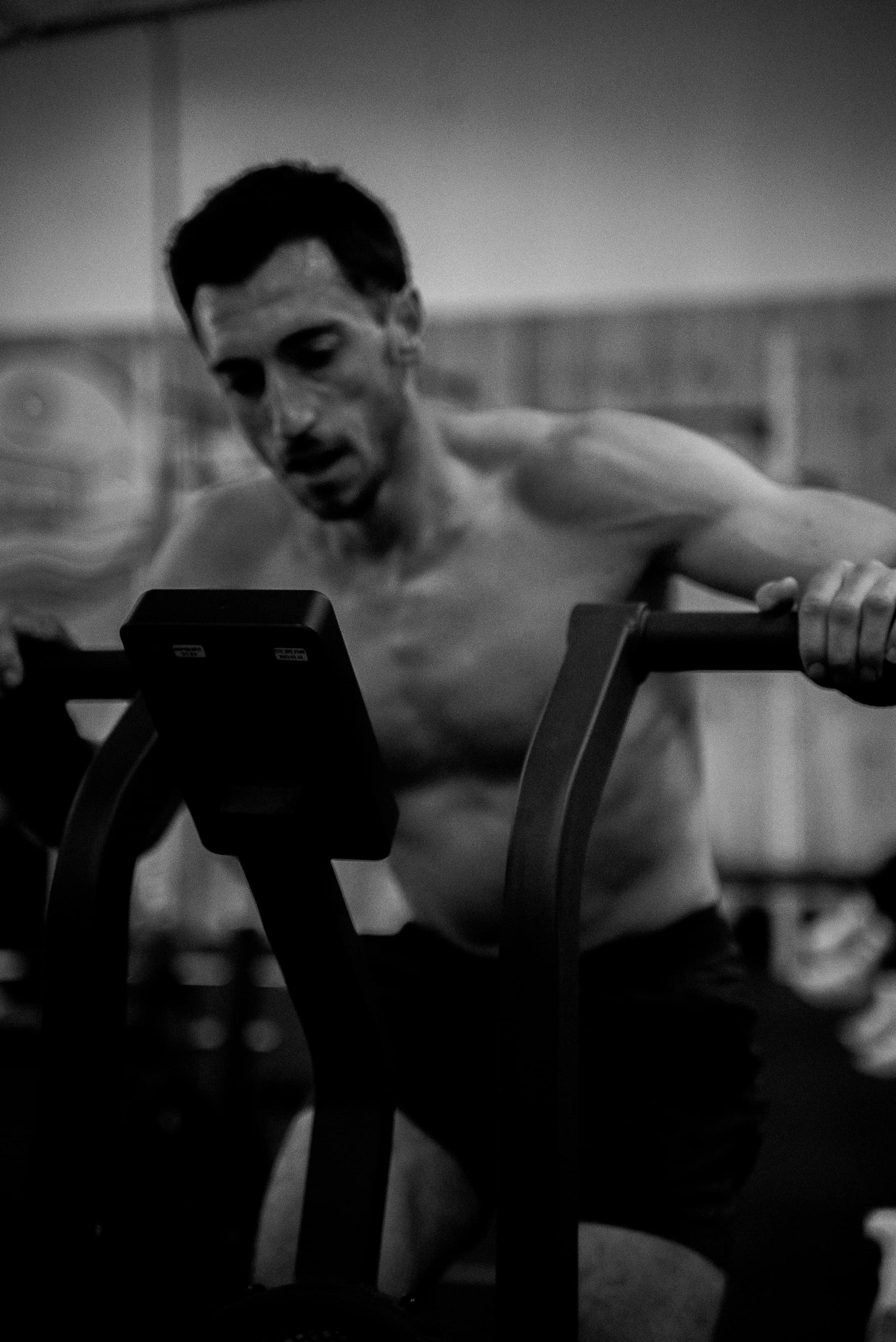 Homme musclé au gymnase, seul, regardant un écran d'écran d'appareil électronique, en noir et blanc.