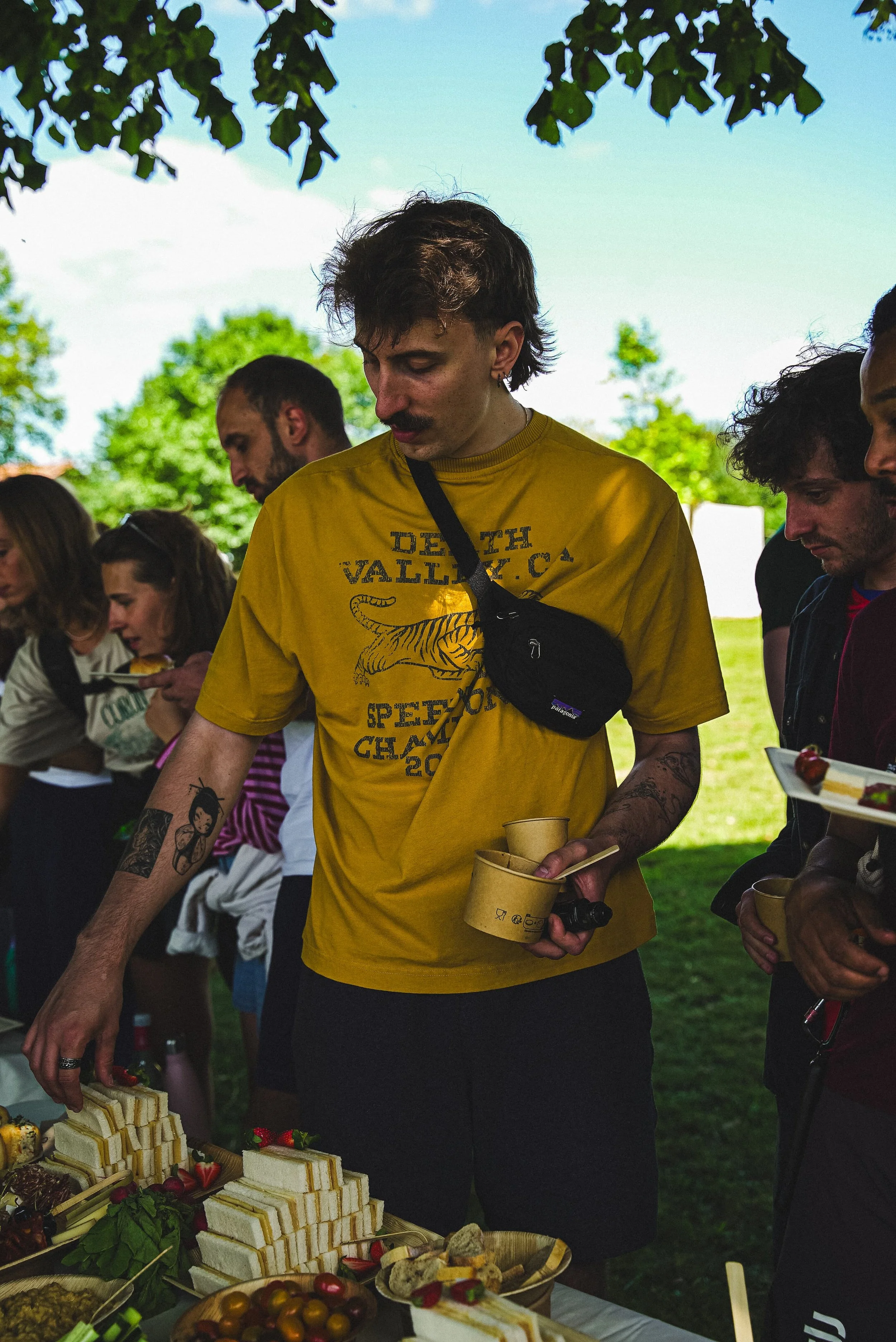 Groupe de personnes autour d'un stand avec des desserts, partageant un moment lors d'un événement en plein air.