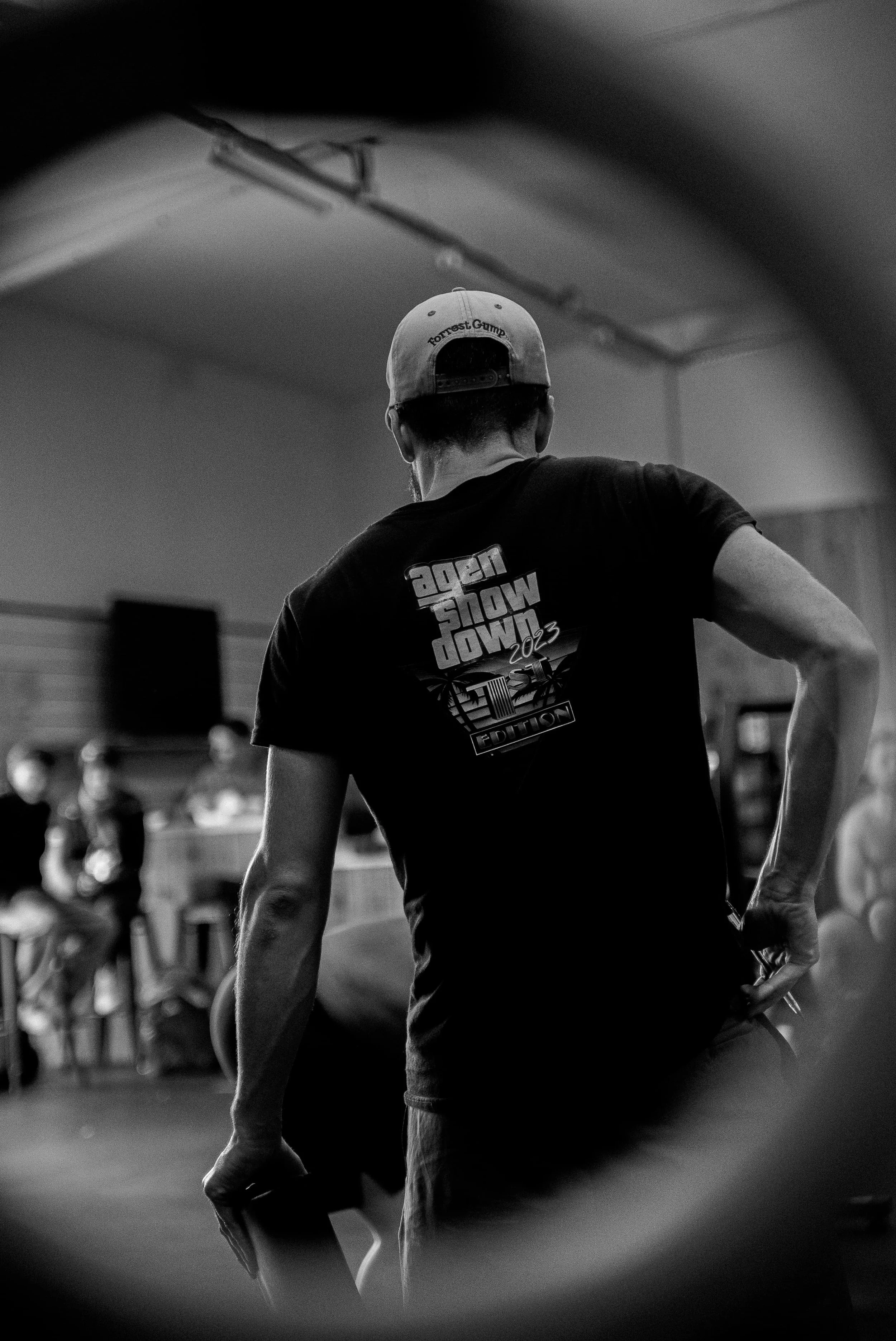 Une personne vue de dos portant une casquette et un t-shirt avec le texte 'Agent Show Down 2023'. Le contexte semble être une salle ou un espace intérieur.