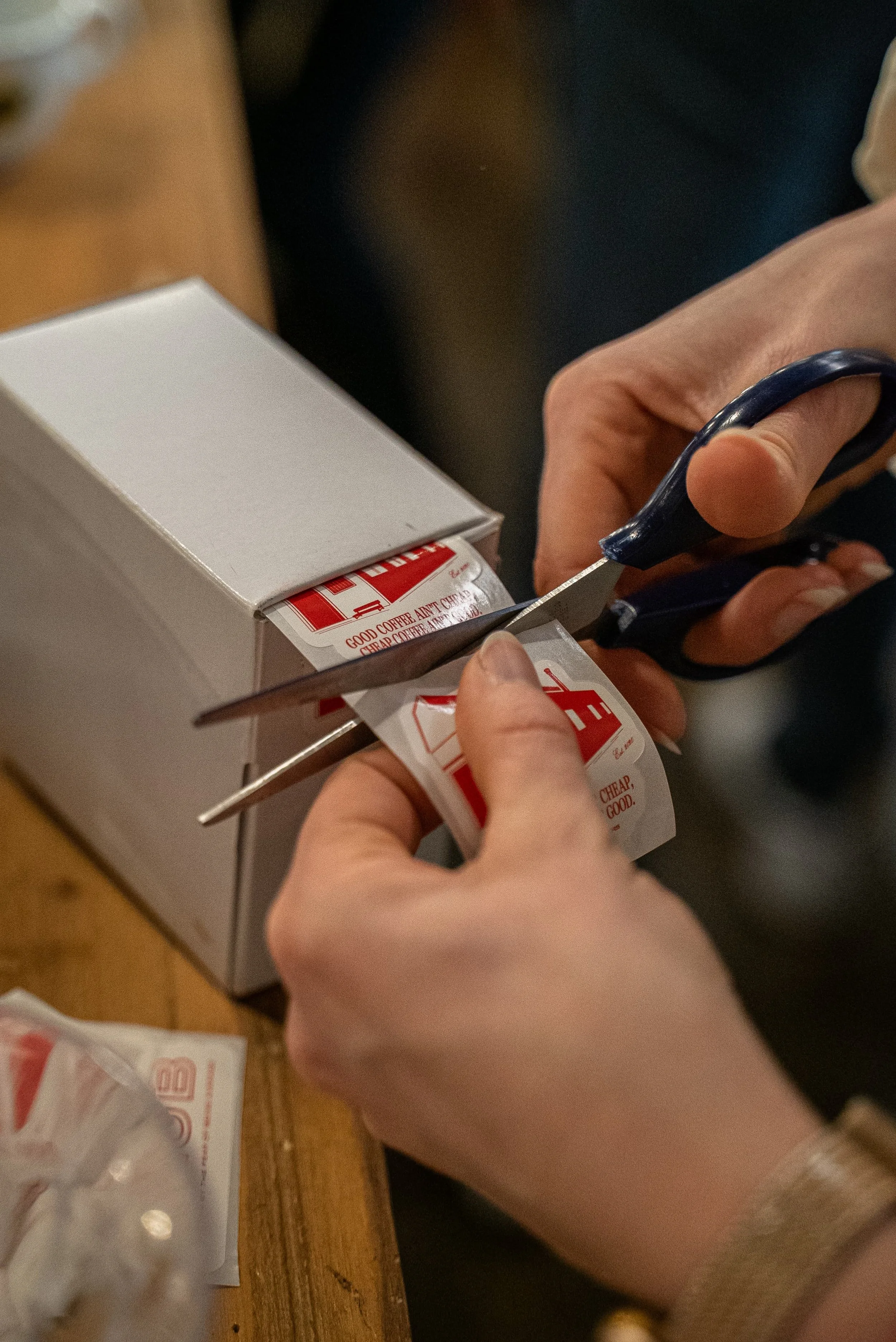Des mains coupant un ticket de caisse avec une paire de ciseaux, avec une boîte blanche et un ticket visible sur une surface en bois.