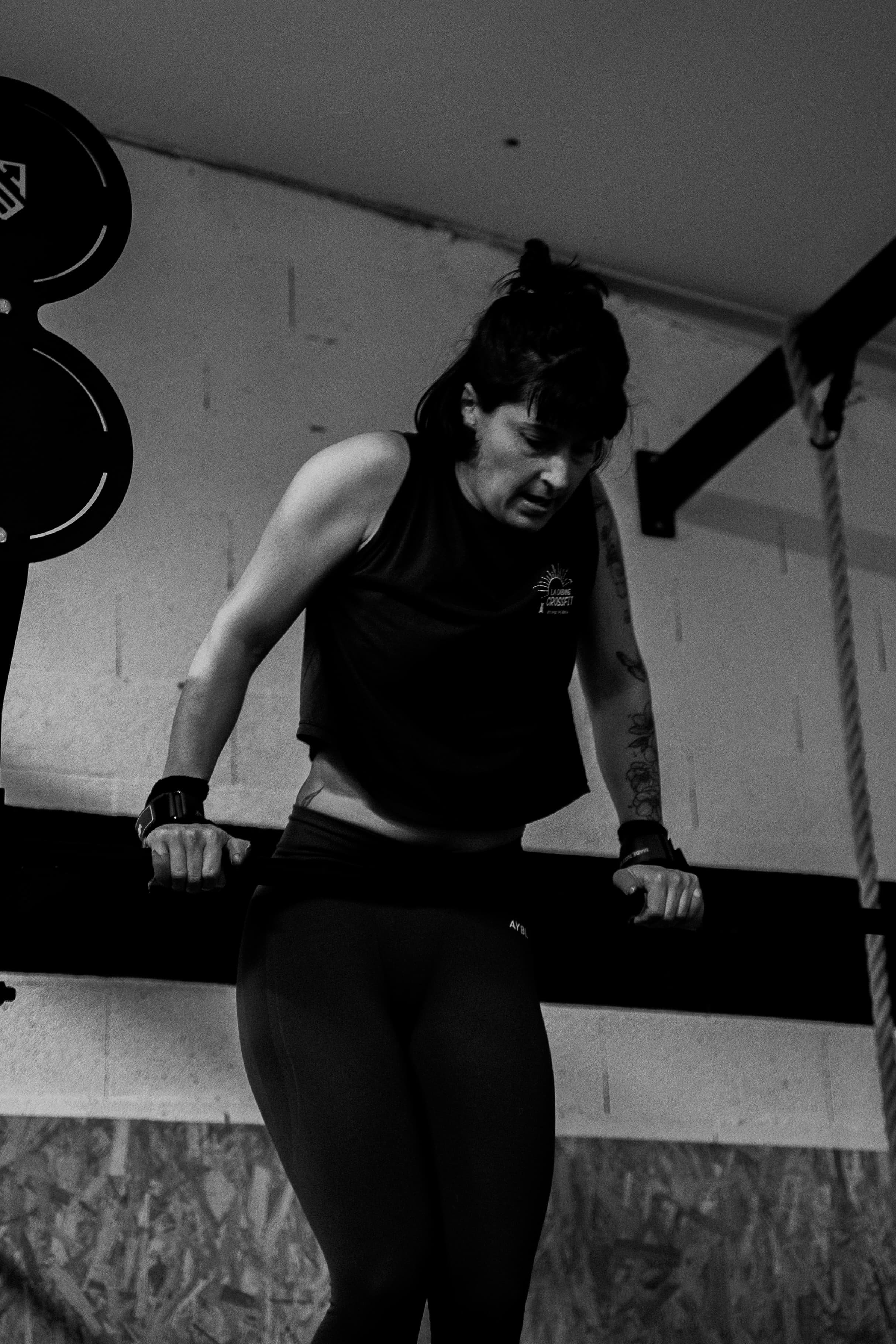 Une femme en tenue de sport effectue un exercice de musculation avec des haltères dans une salle d'entraînement. Elle semble concentrée sur son effort.