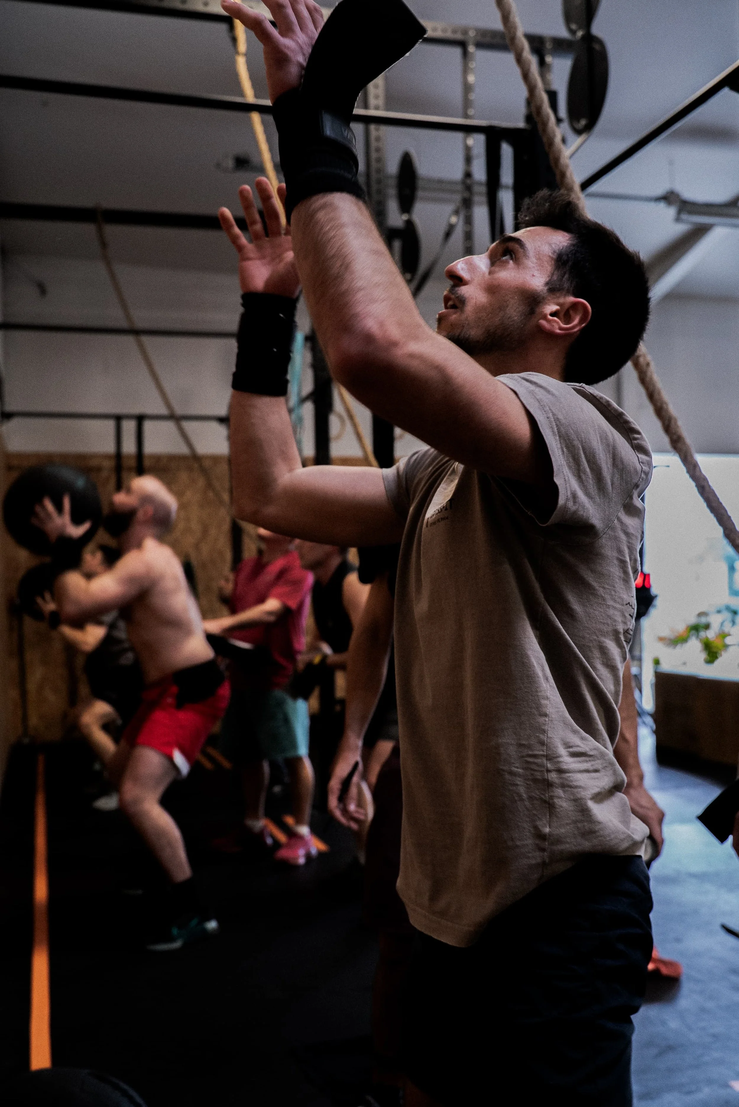 Un homme faisant de l'exercice dans une salle de sport, debout avec un bras levé et tenant un objet, avec plusieurs autres personnes en arrière-plan également en train de faire de l'exercice.