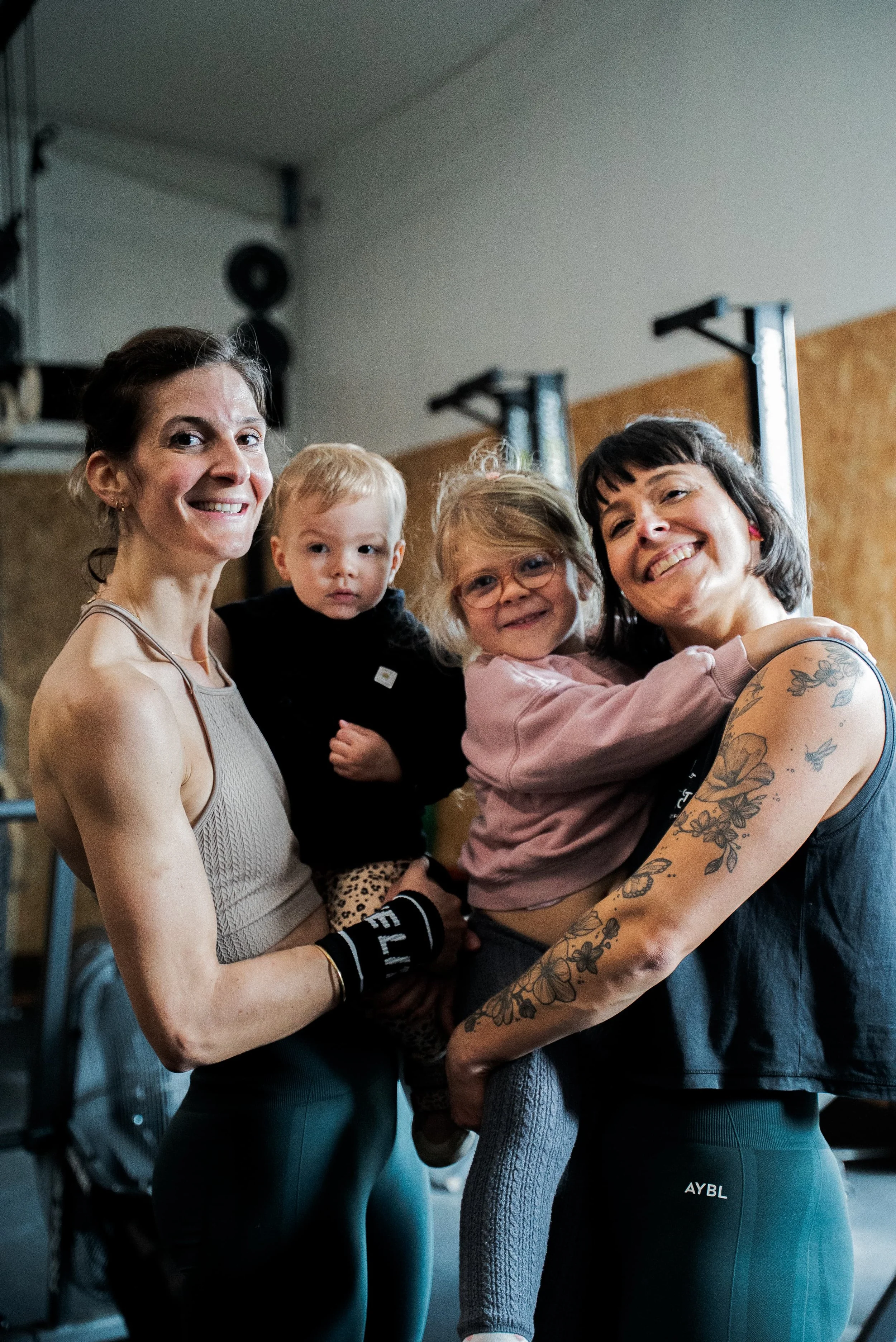 Deux femmes et deux jeunes enfants dans une salle de sport, souriants et célébrant ensemble après une séance d'entraînement.